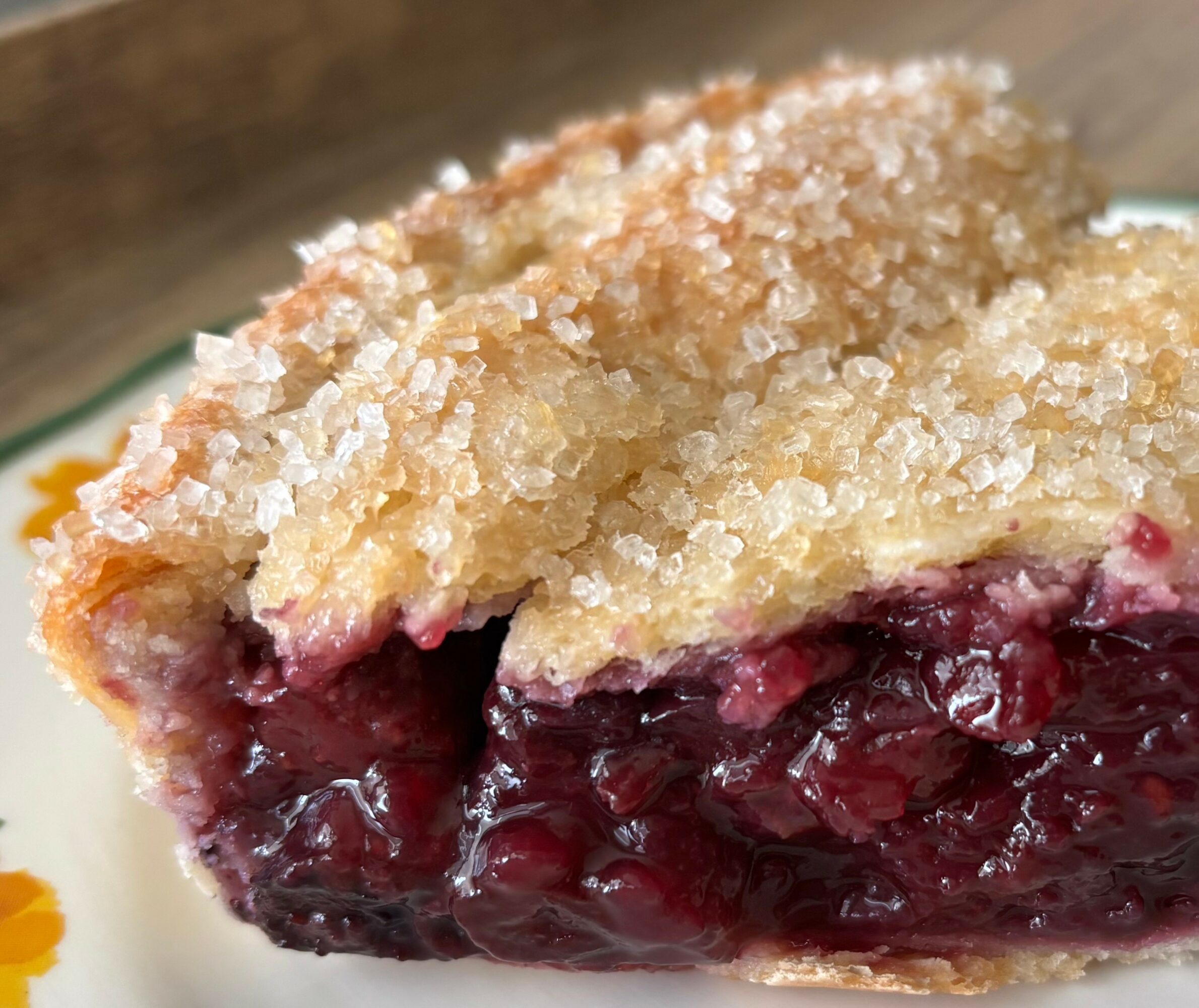 Close-up of a slice of pie with a golden crust and dark berry filling, on a plate.