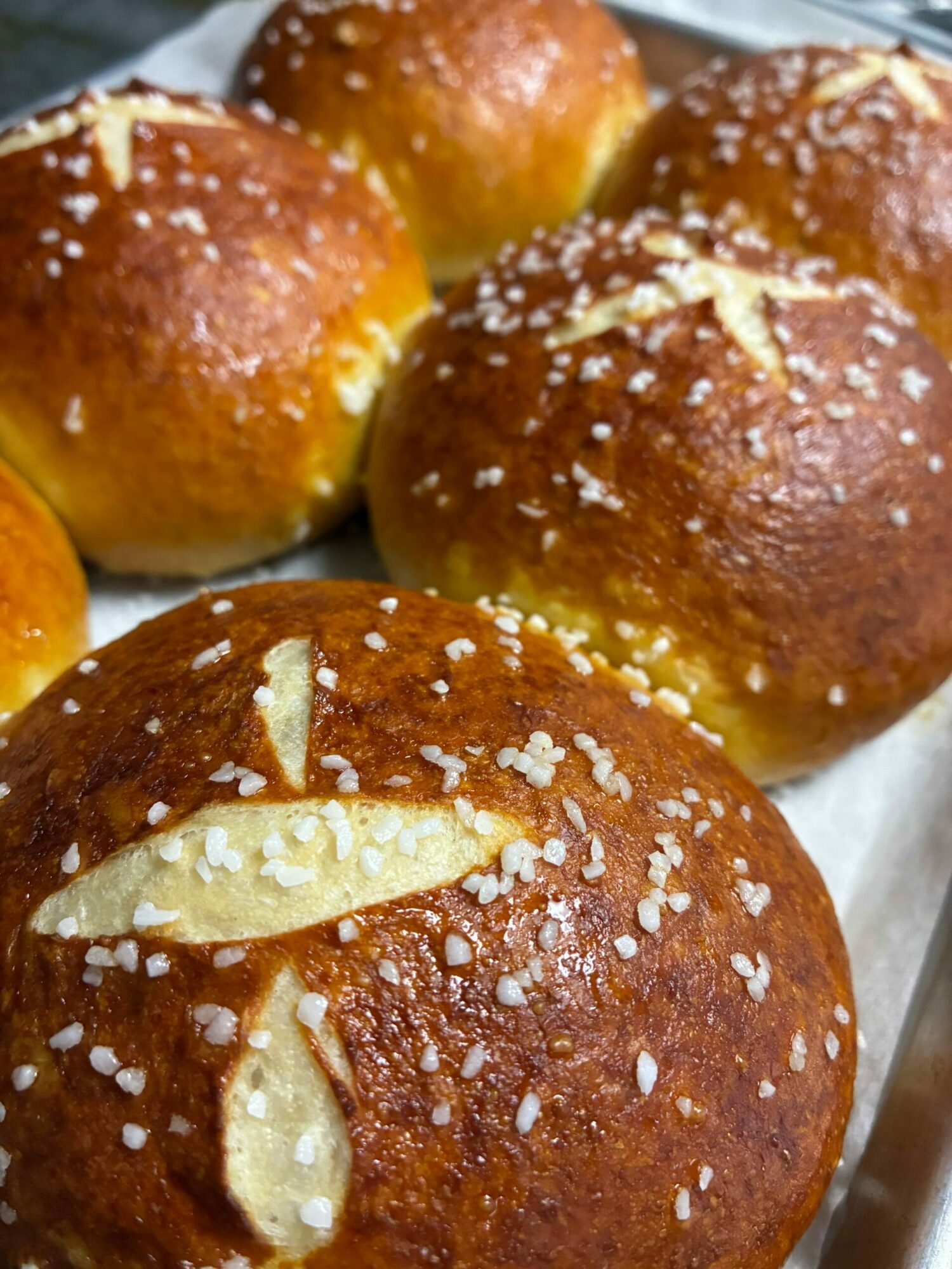 Close-up of four golden-brown bread rolls with sugar crystals, some topped with almond slices, on a white surface.