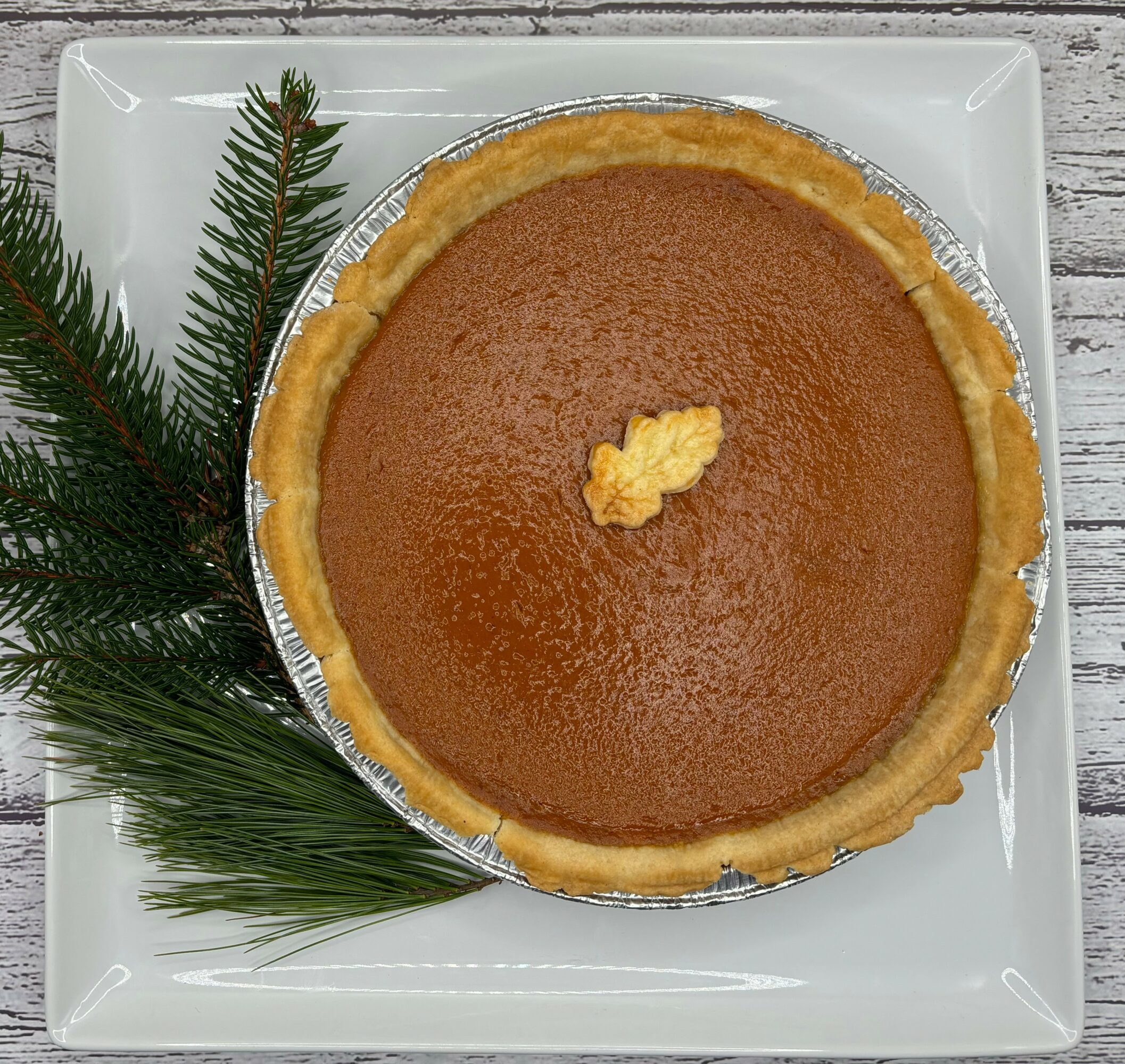 Pumpkin pie on a white plate with pine branches, top view, with a dollop of whipped cream in the center.