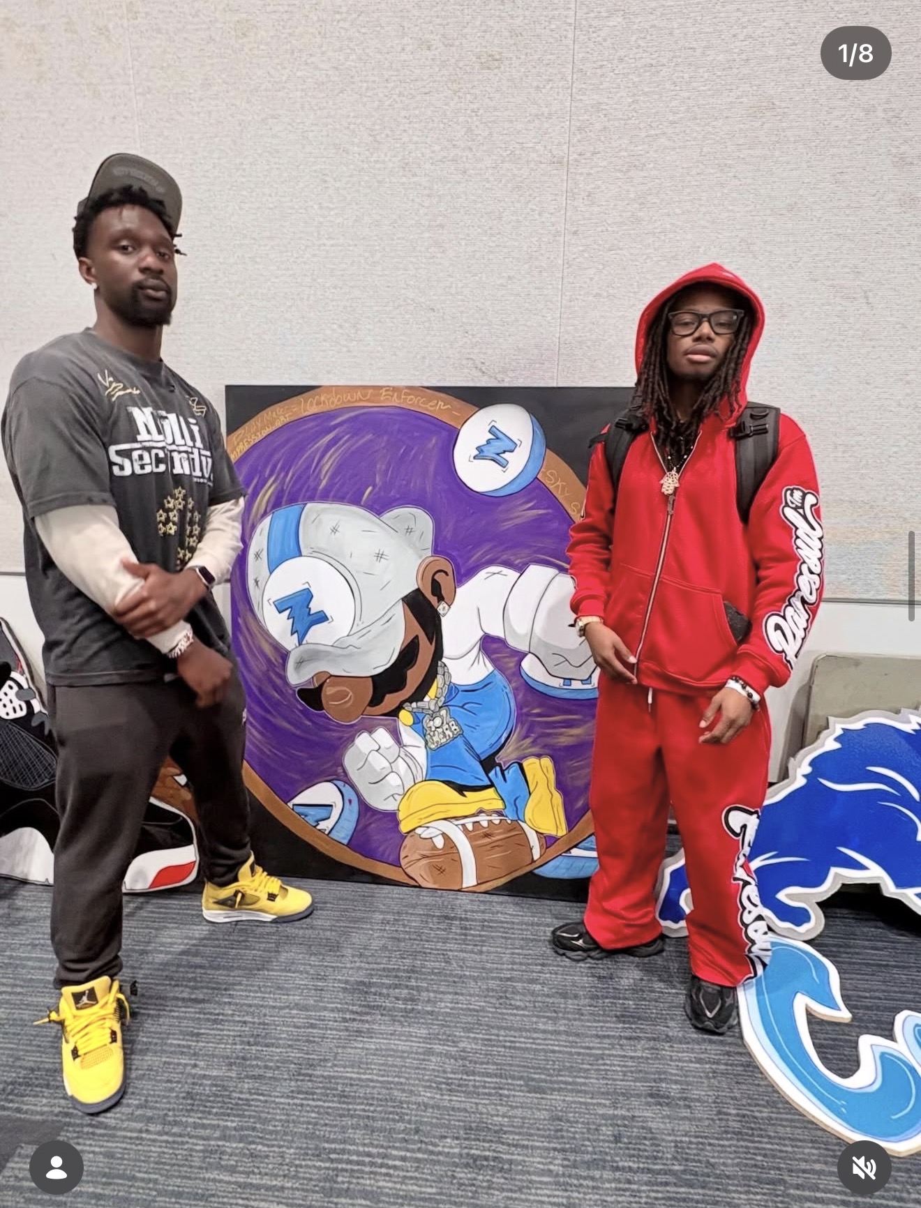Two people standing next to a colorful cartoon character painting on a circular canvas, in an indoor setting.