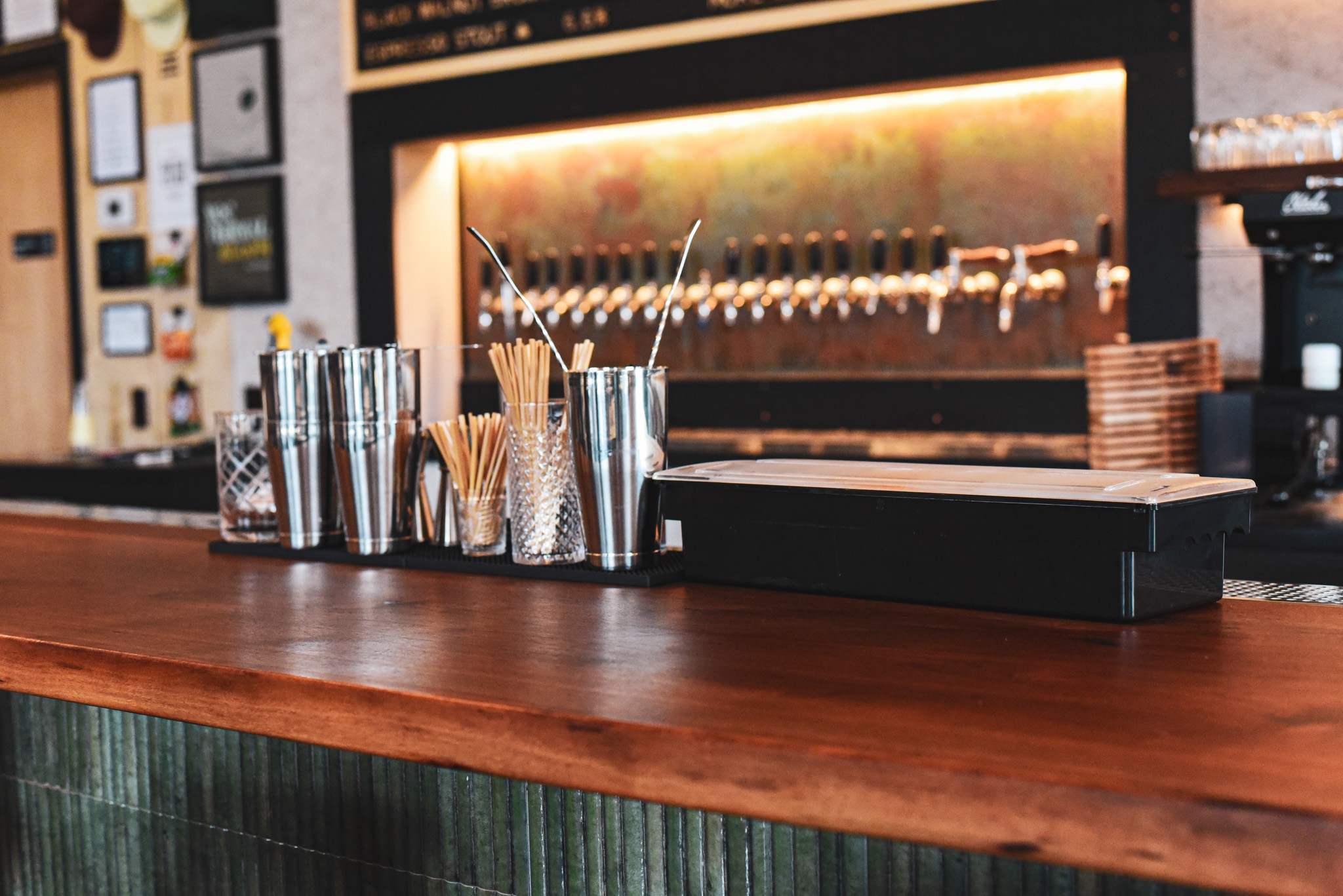 Bar counter with metal containers holding straws and stirrers, and a row of beer taps in the background.