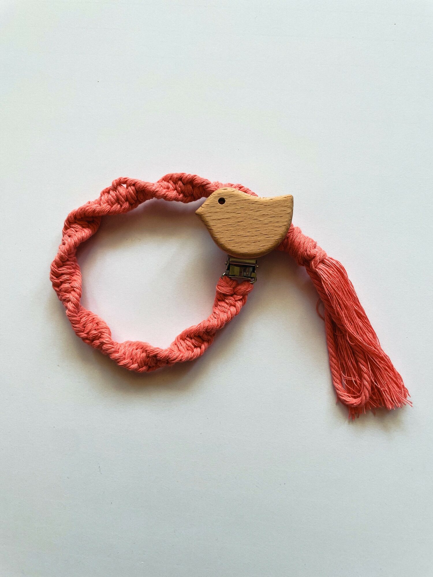 Pink braided cord with a wooden bird-shaped ornament and a tassel, on a white background.