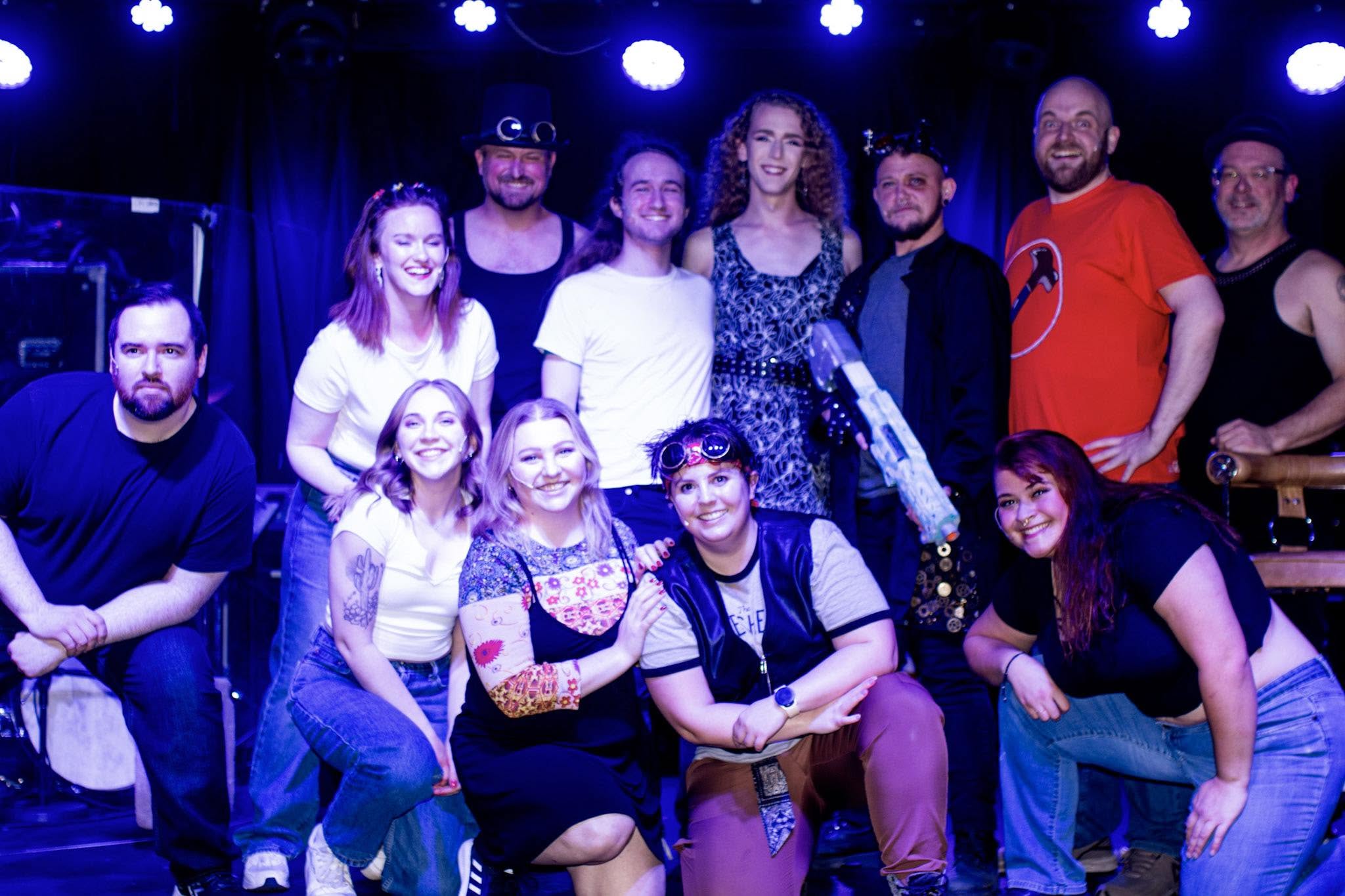 Group of people posing on stage with blue lighting, some smiling, some with serious expressions, diverse in appearance.