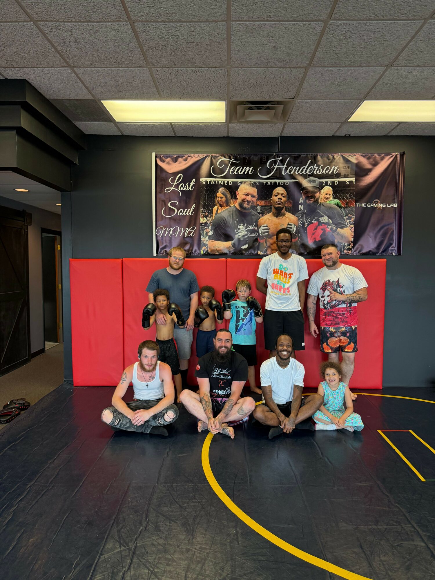 Group of people posing in front of a banner, some sitting and some standing, in an indoor setting.