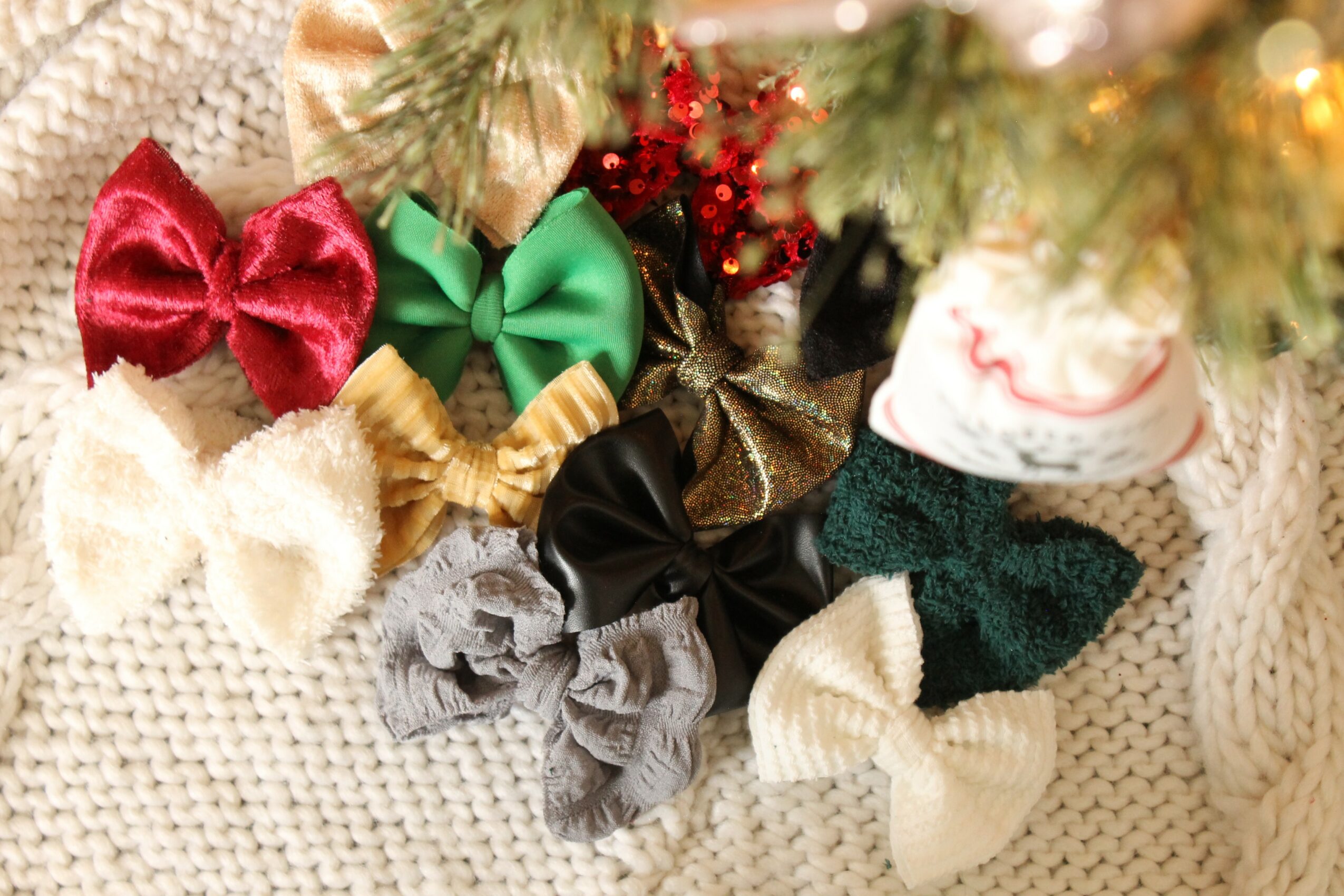 Various colorful bows and ribbons arranged on a knitted surface with Christmas decorations in the background.