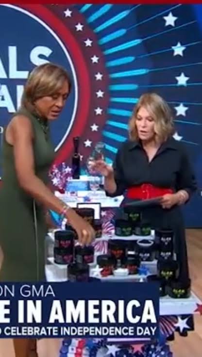 Two women stand at a table with patriotic decorations and products, celebrating Independence Day on a television show set.