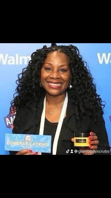 Woman with curly hair smiling, holding a congratulatory card and a small yellow object, against a blue background.