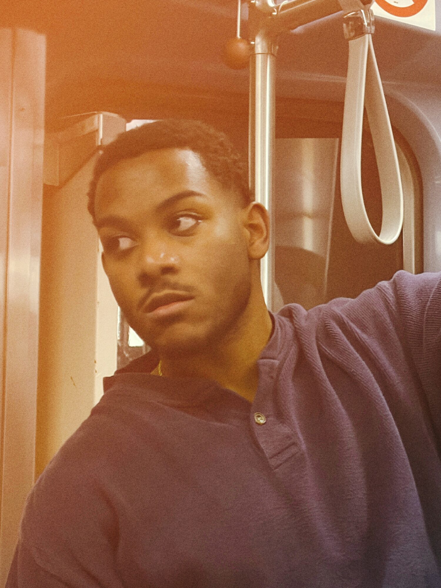 Young man with short hair looking to the side, wearing a dark shirt, inside a bus or train, holding onto a strap.