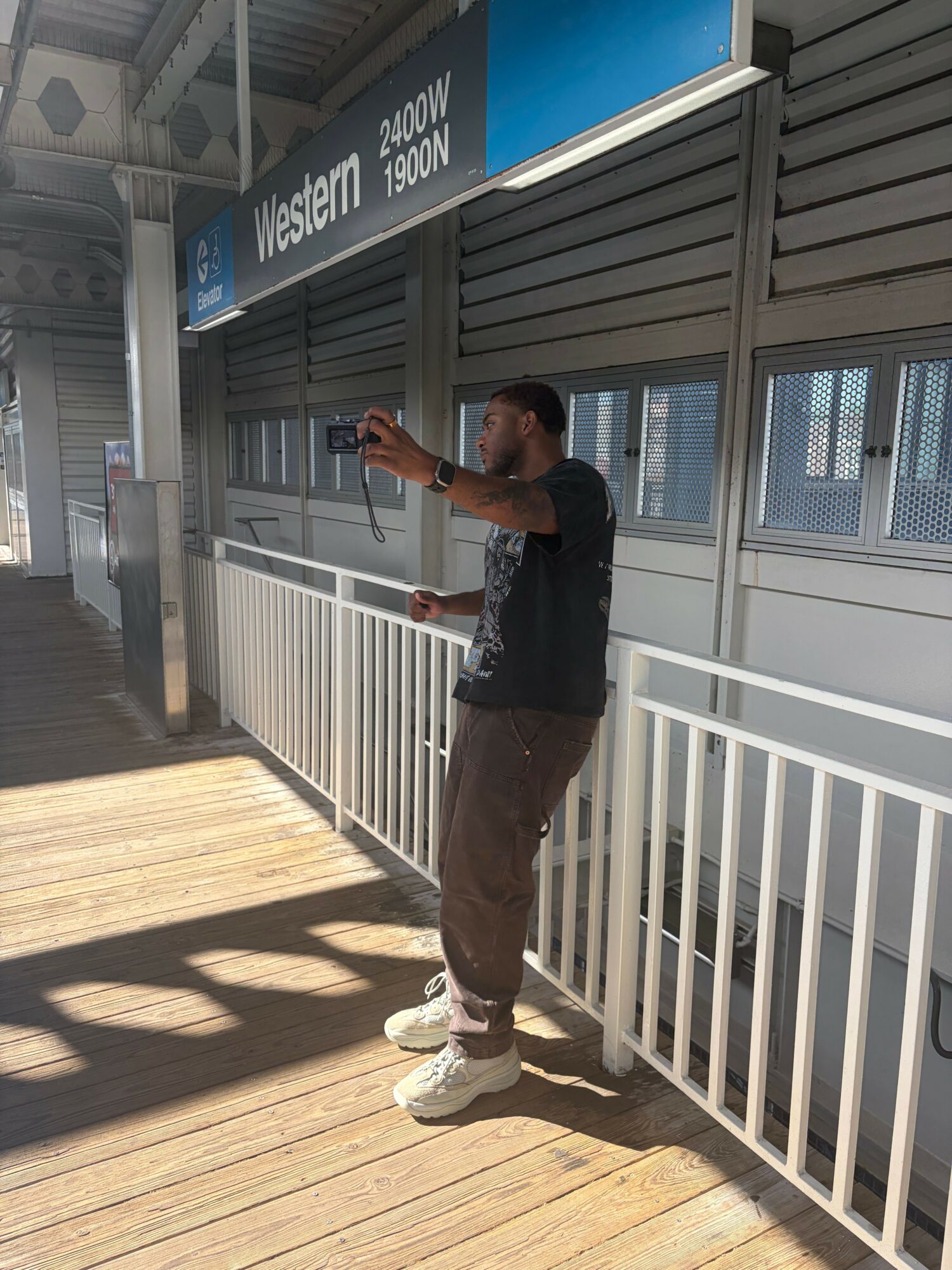 Person leaning on railing on a balcony with wooden floor and building exterior in background.