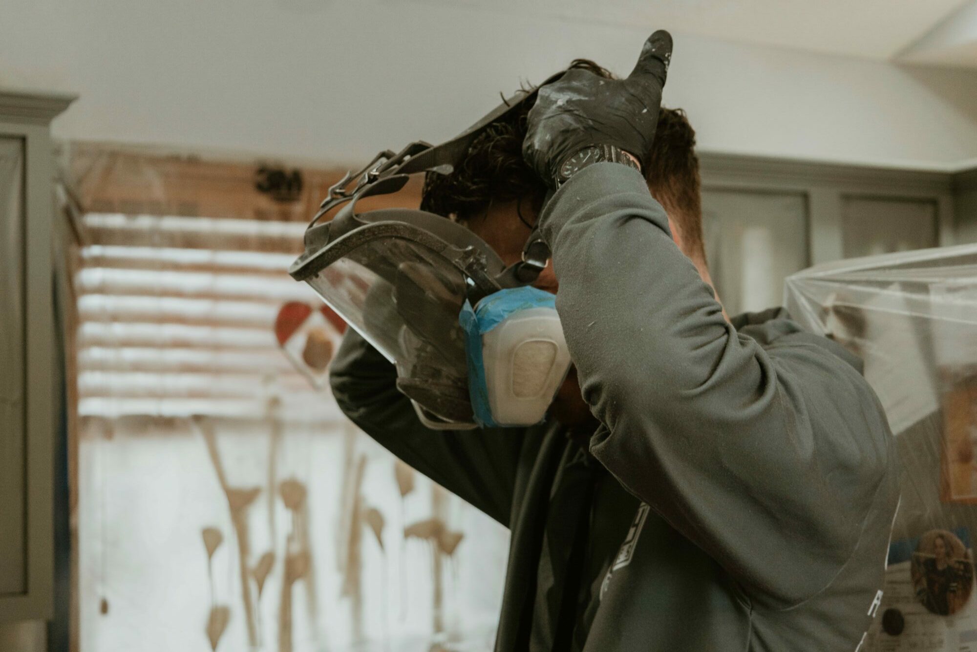 Person wearing protective gear, including a helmet and mask, adjusting their helmet inside a room.