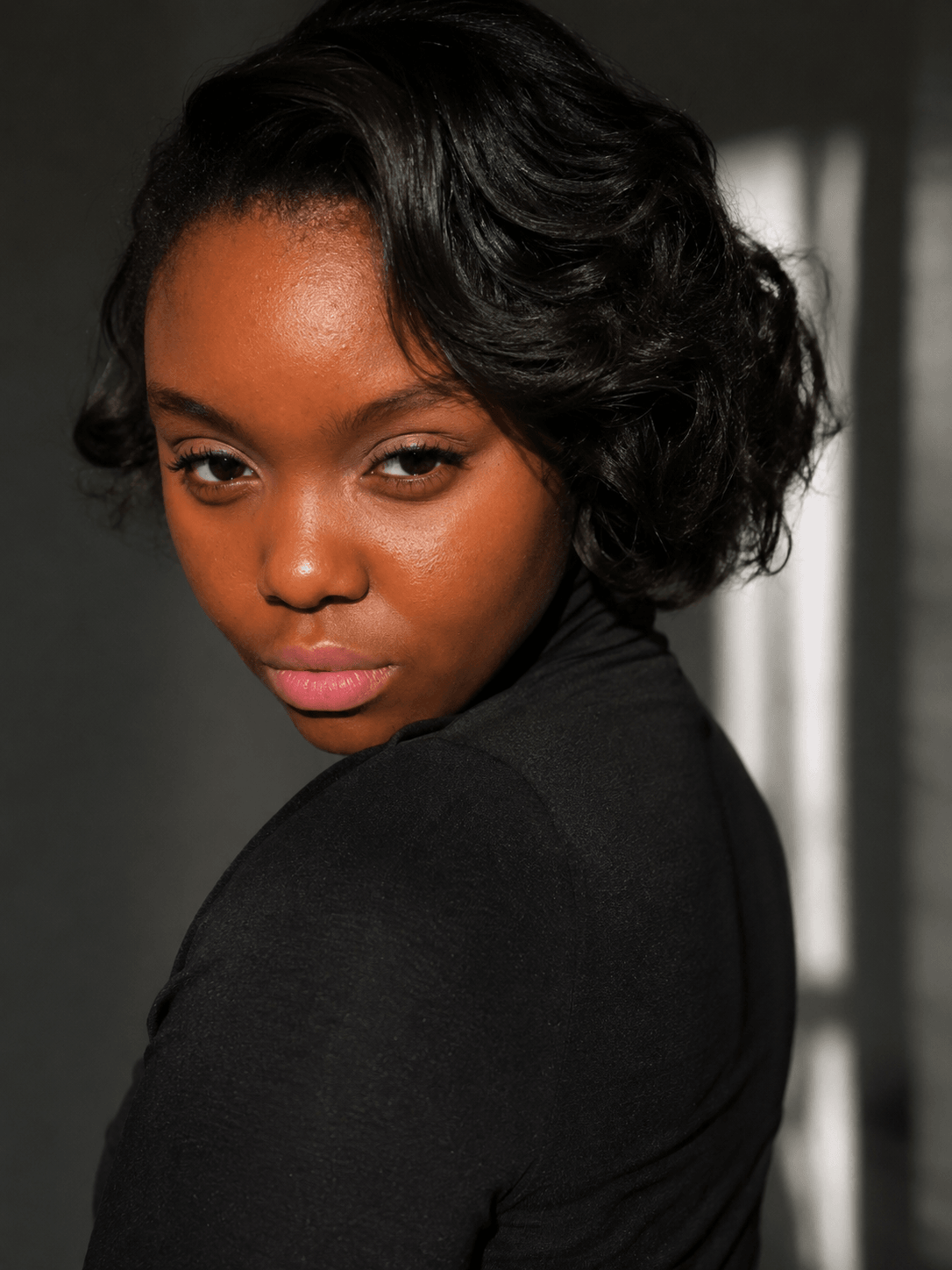 Portrait of a woman with short, wavy hair, looking confidently at the camera, wearing a black top.