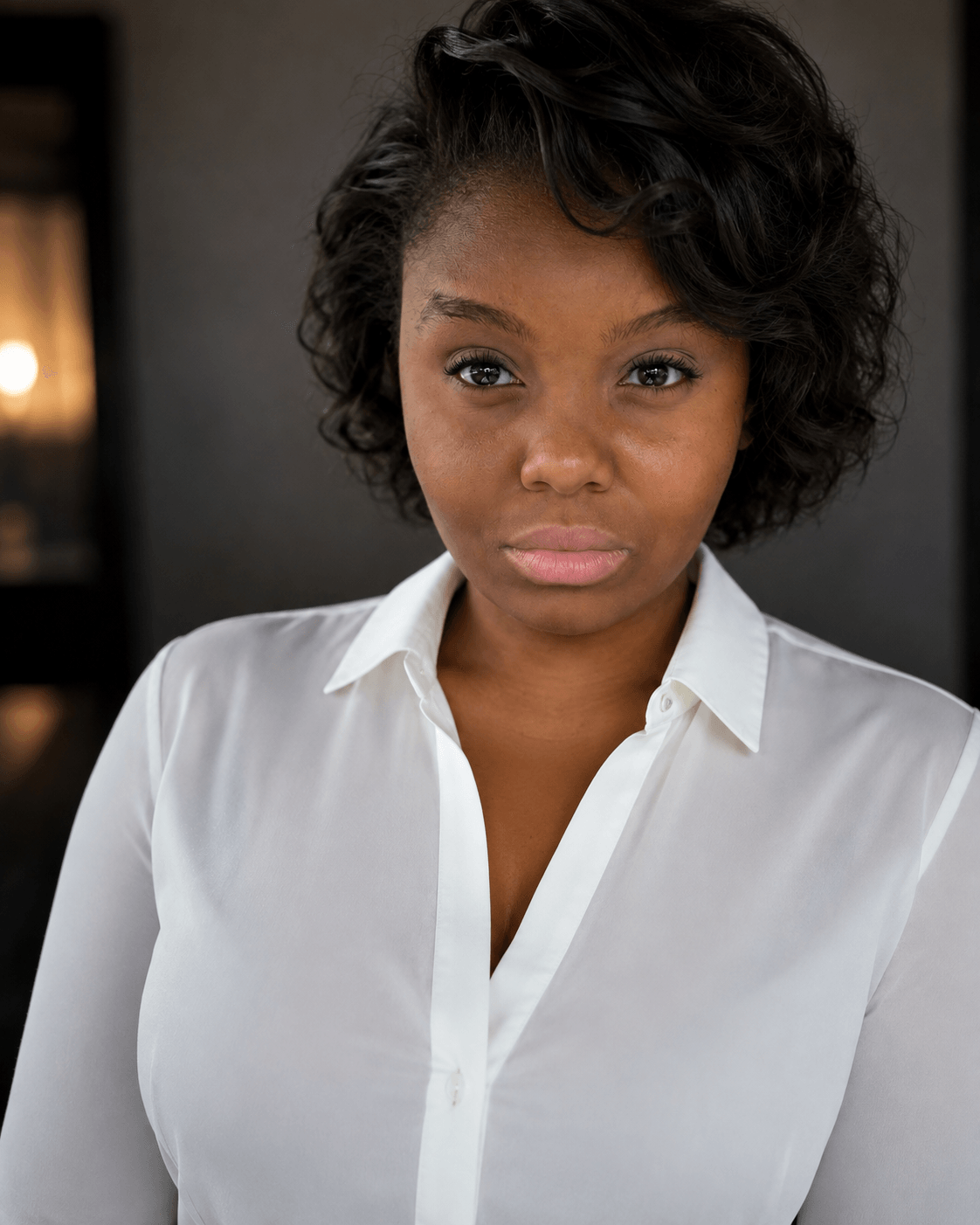 Portrait of a woman with short, curly hair wearing a white shirt, looking slightly to the side.