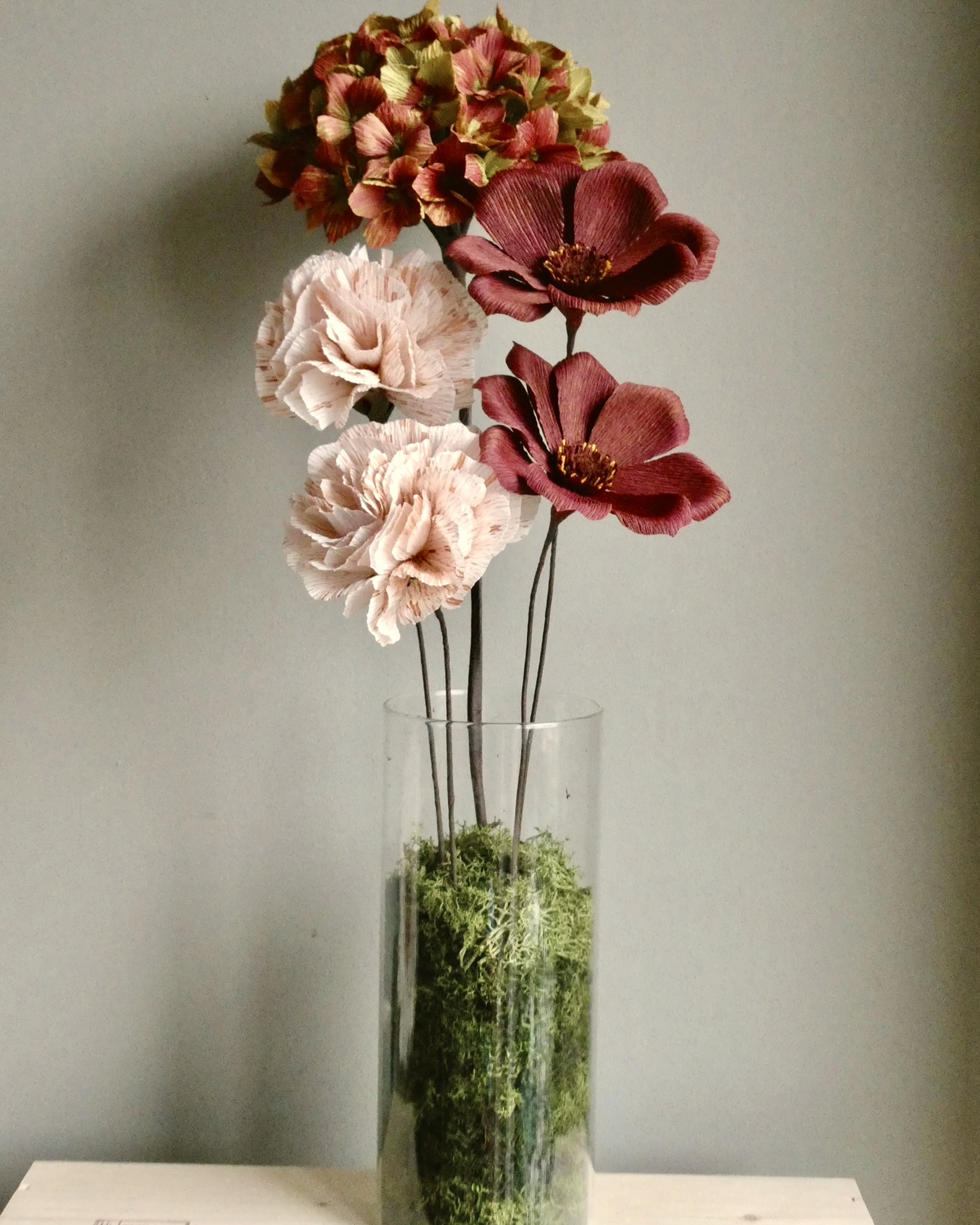 Vase with pink, red, and green flowers on a table against a plain wall.