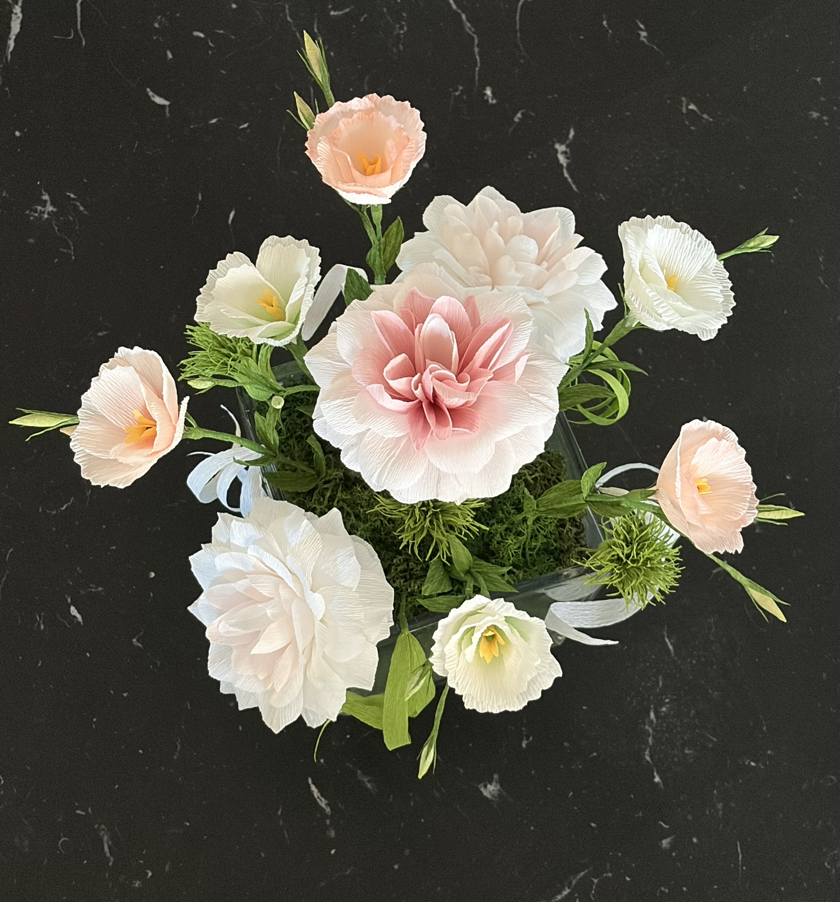 Arrangement of pink, white, and cream flowers with green leaves on a dark background.
