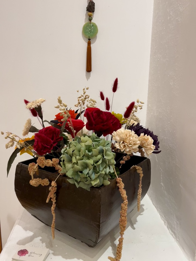 Flower arrangement with red, white, and purple flowers in a black rectangular container, placed on a white surface against a white wall.