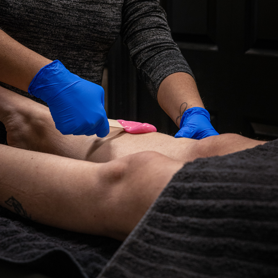 Person in gray shirt and blue gloves performing a medical procedure on a patient's leg, with a pink tool.
