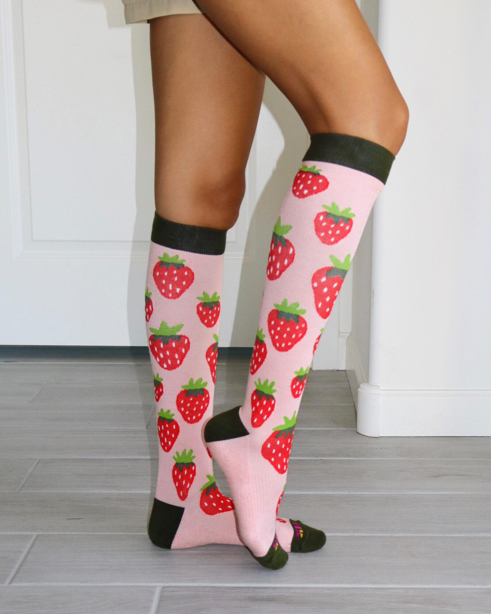 Person wearing knee-high socks with strawberry patterns, standing on a wooden floor, with a white door in the background.