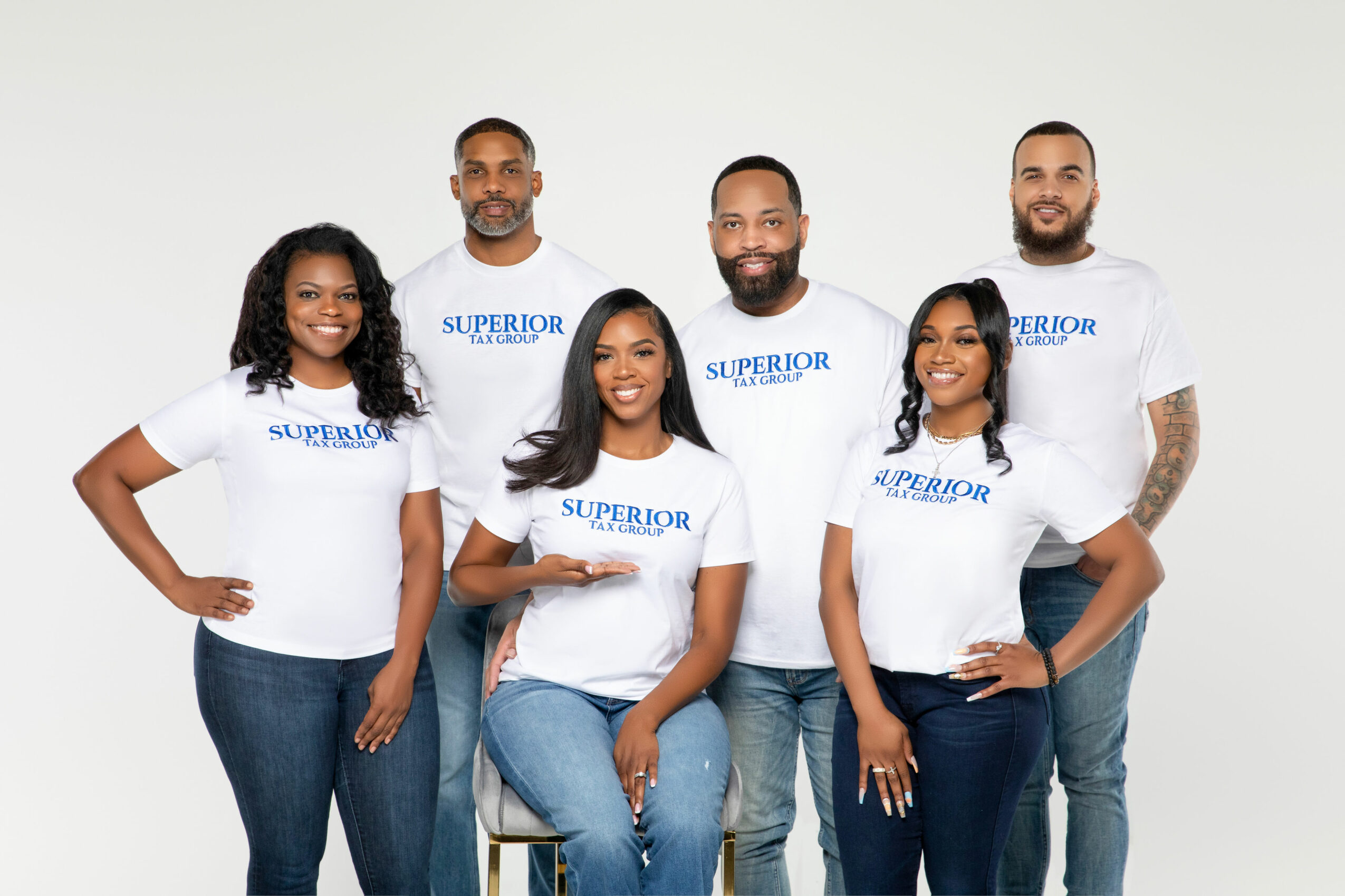 Group of six diverse people wearing white T-shirts with blue text, standing against a plain background.