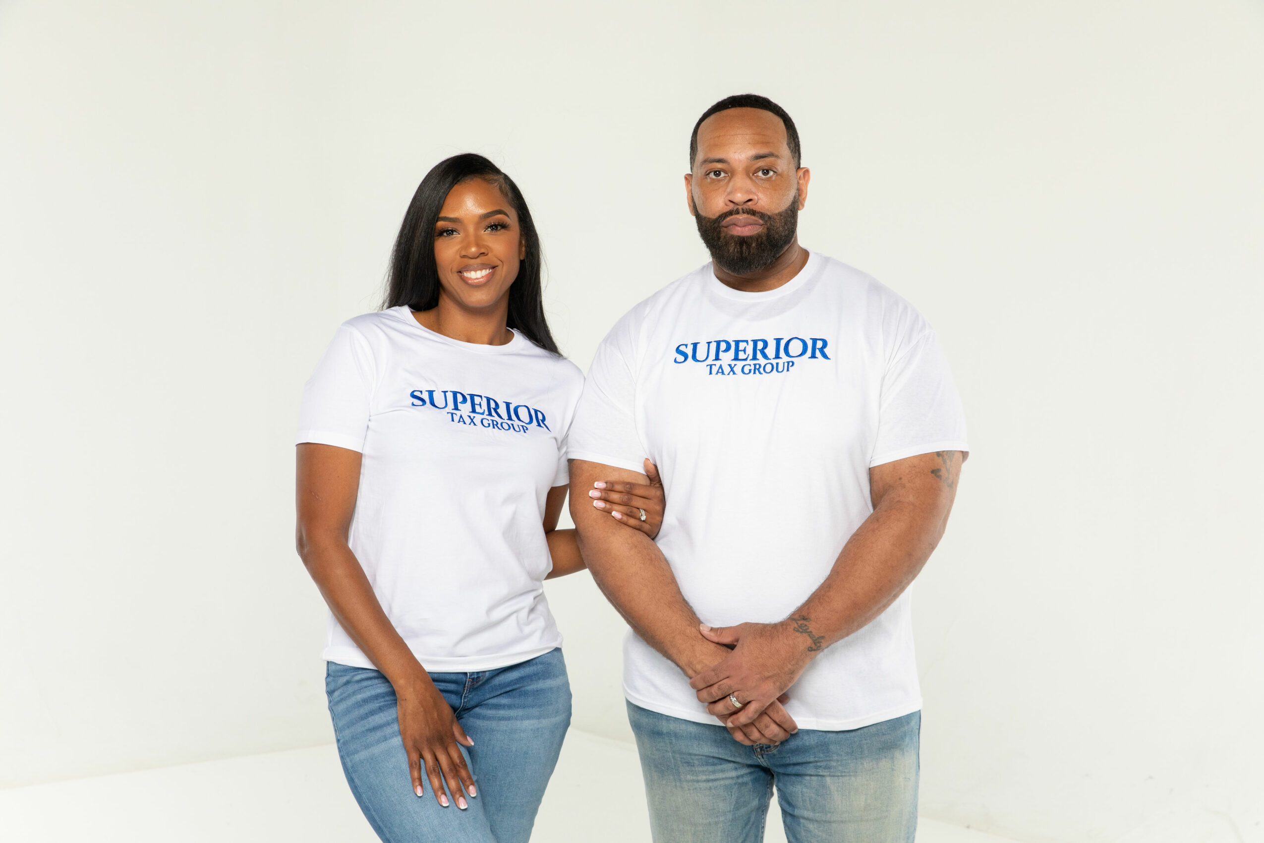 Two people stand side by side wearing white t-shirts with blue text, smiling, against a plain white background.