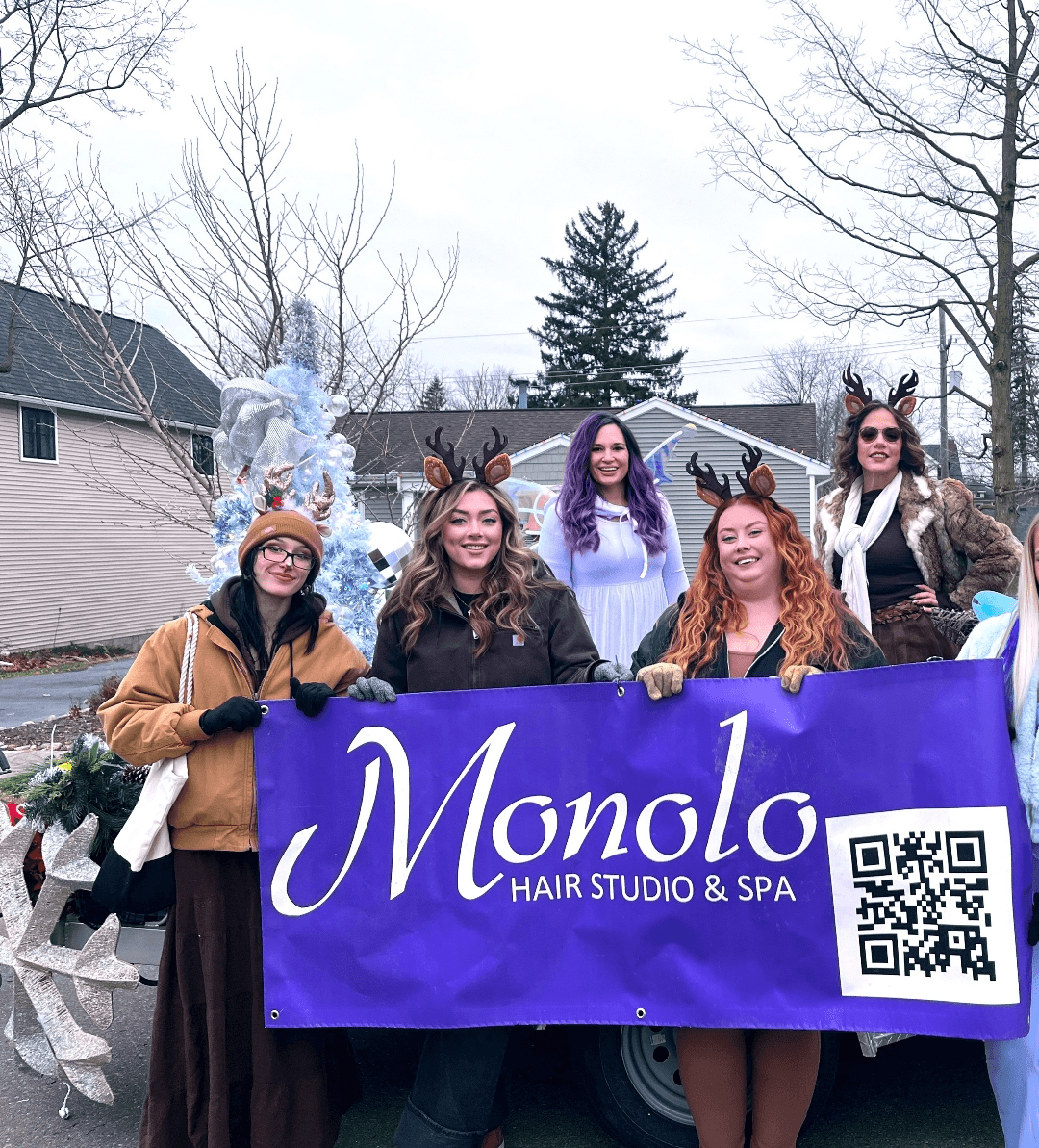 Group of five women holding a purple banner with 'Monolo Hair Studio & Spa' and a QR code, outdoors with trees and buildings.