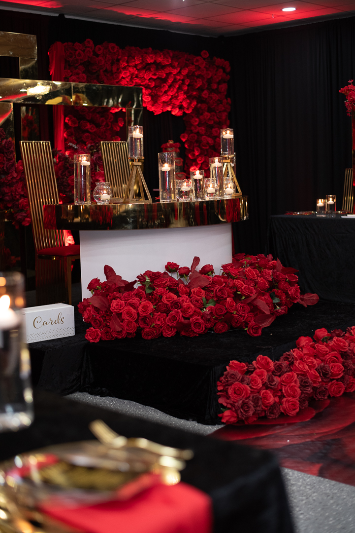 Table decorated with red roses, candles, and gold accents in a dimly lit setting, possibly for a celebration or event.
