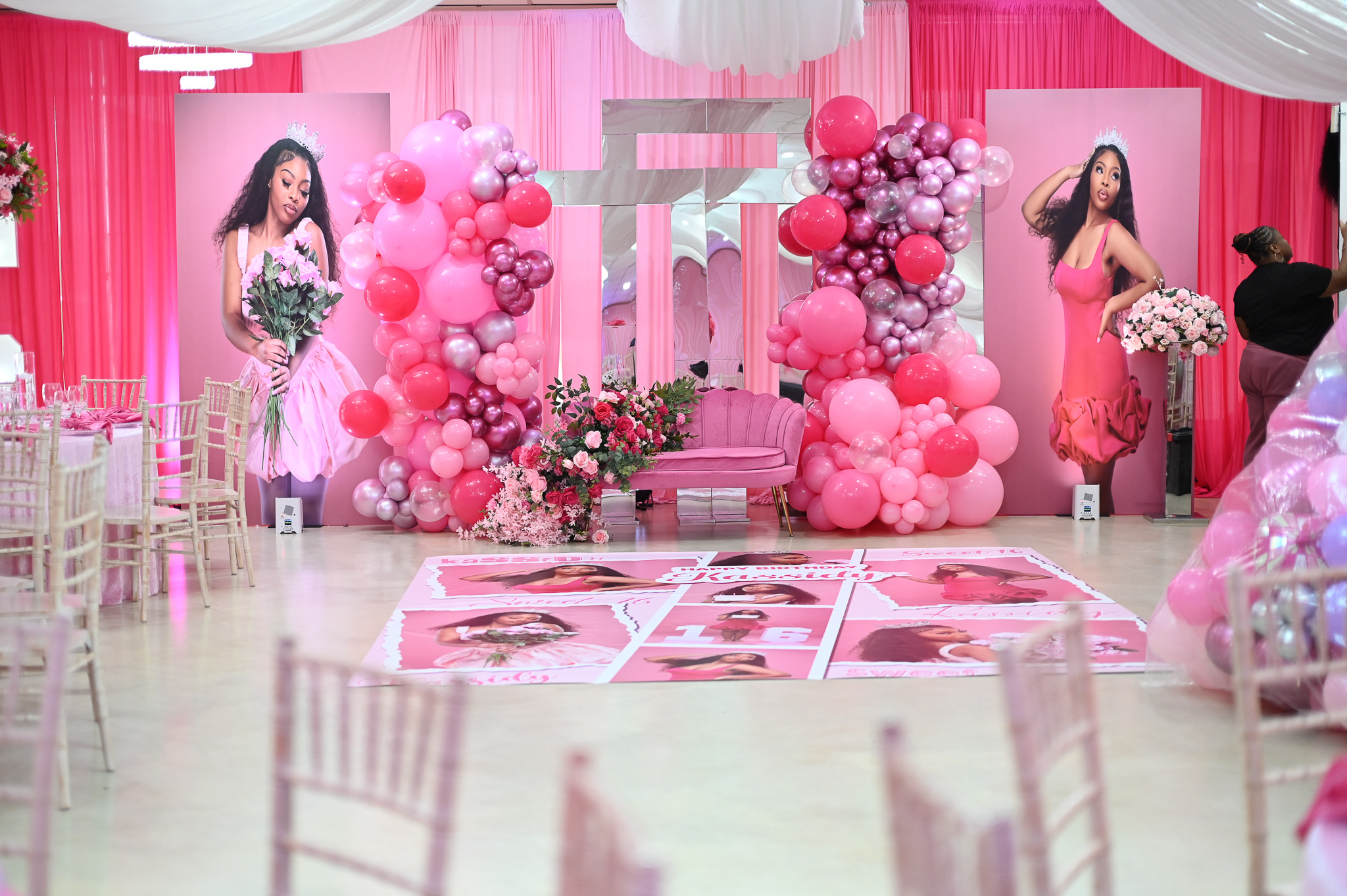 Decorated event space with pink balloons, flowers, and two women in pink dresses, with chairs and a pink backdrop.