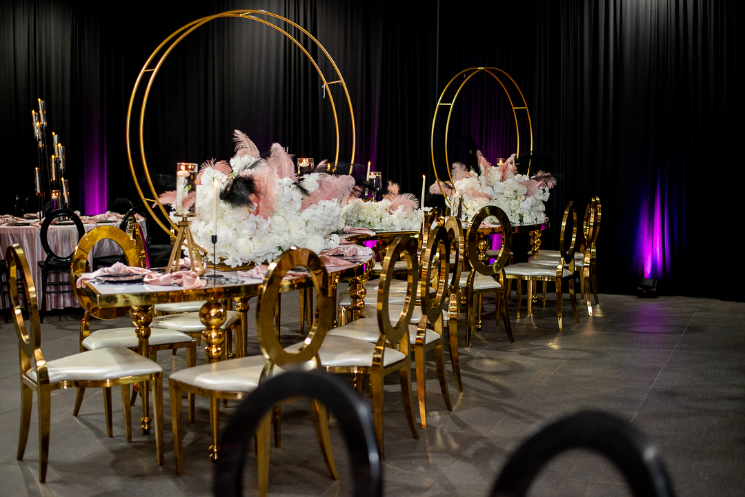 Elegant event table with gold chairs, floral centerpieces, and circular gold decorations on a dark backdrop with purple lighting.