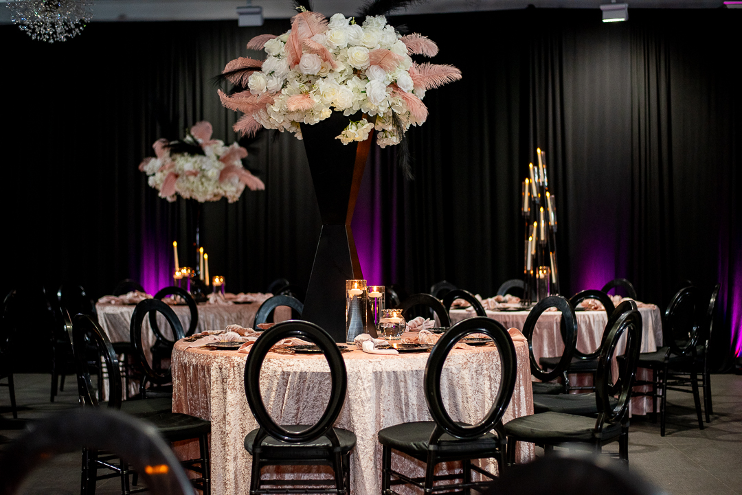 Elegant banquet table with floral centerpiece, candles, and black chairs in a decorated event space.