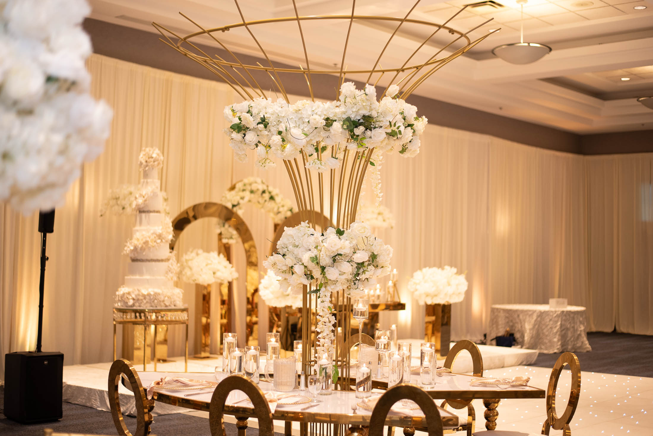 Elegant event space with tall floral centerpieces, gold accents, and draped walls, decorated for a celebration or wedding.