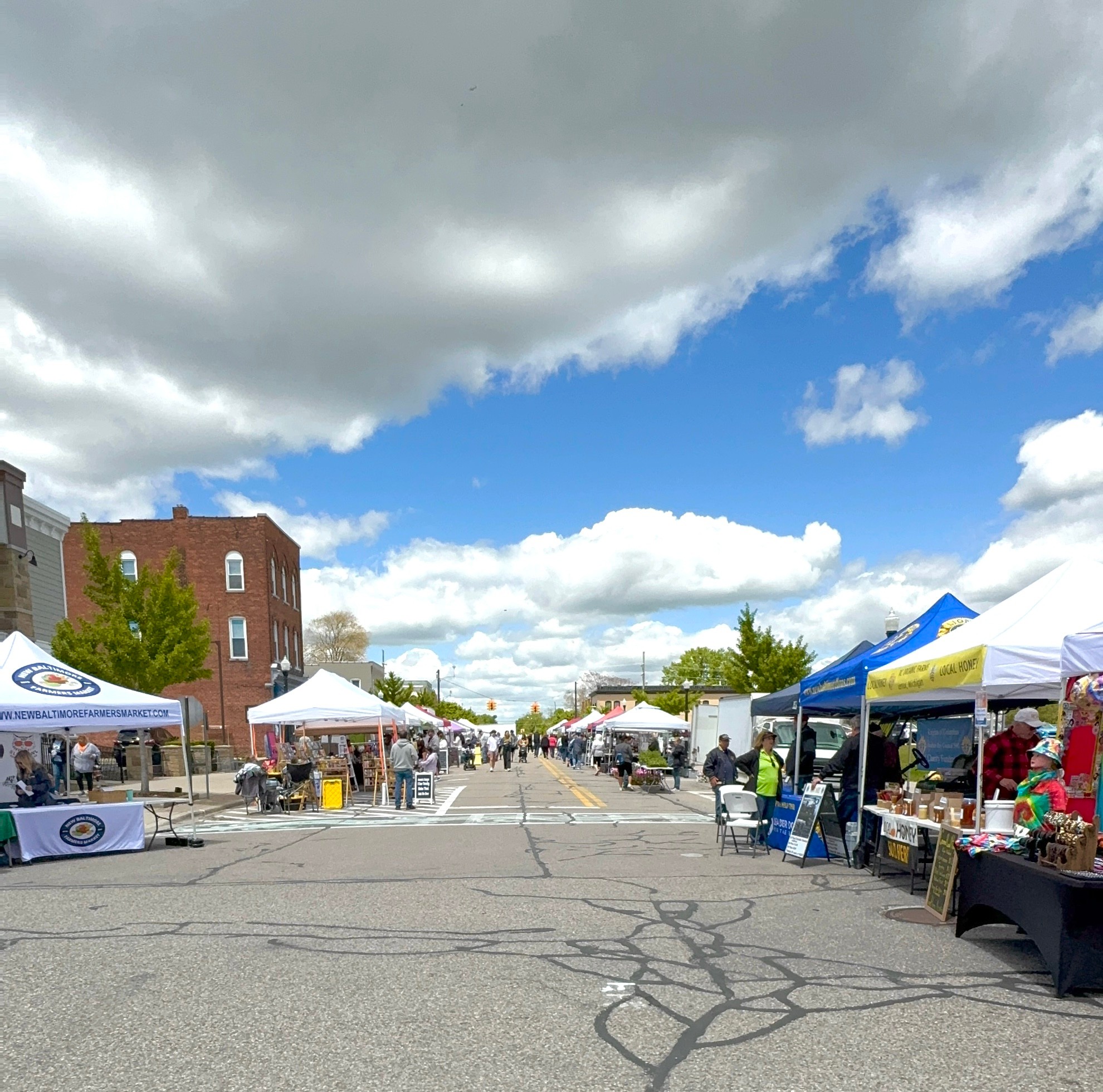 Outdoor market with tents and stalls on a street, cloudy sky with patches of blue, buildings in the background.