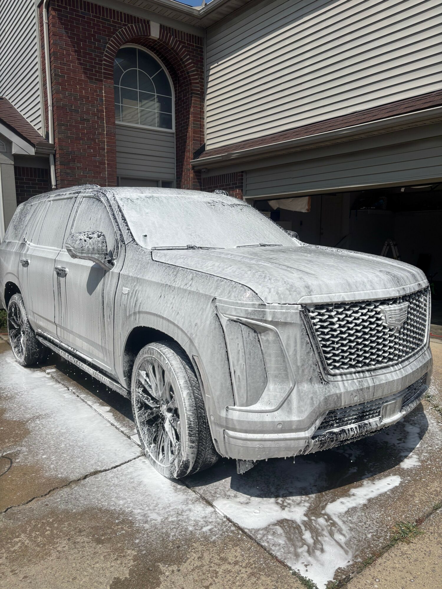Silver car parked outside a house with snow on the ground, partially covered in snow, next to a brick wall and garage.
