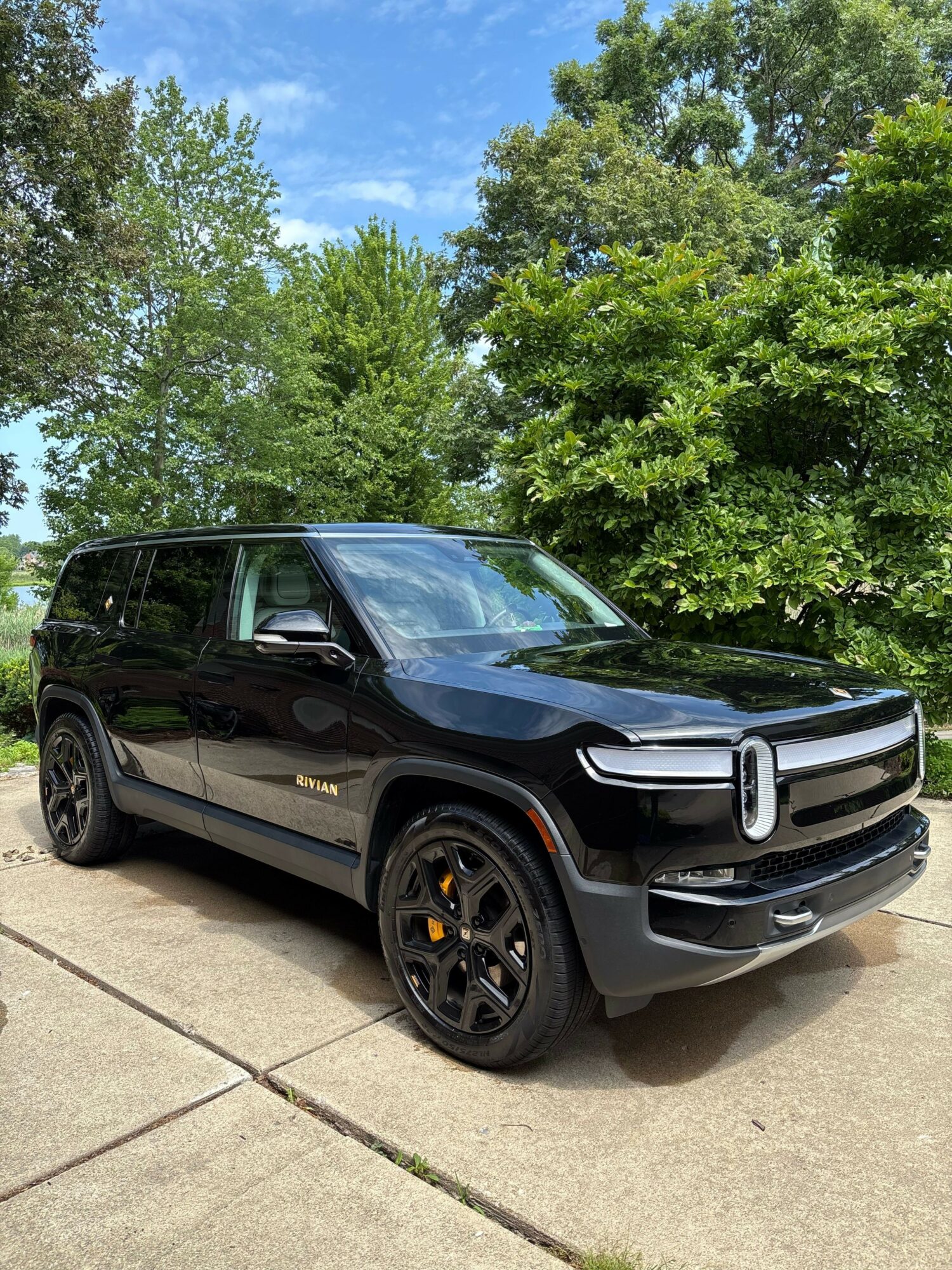 Black and gray car parked on a driveway with green trees and blue sky in the background.