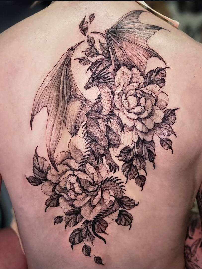 Dragon with wings surrounded by large blooming flowers and leaves on person's back.