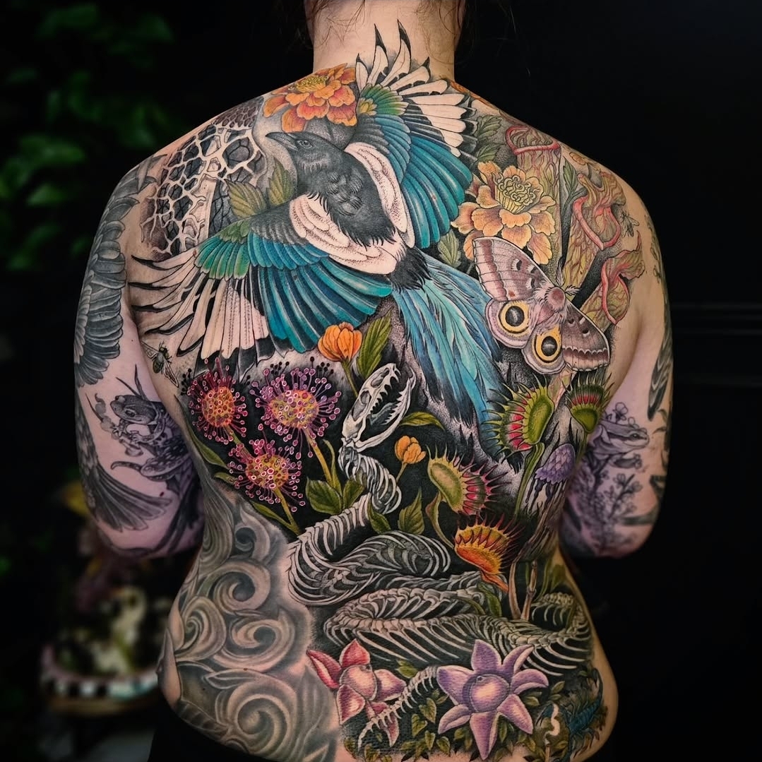 Colorful back tattoo featuring birds, flowers, and butterflies with intricate details and vibrant colors.