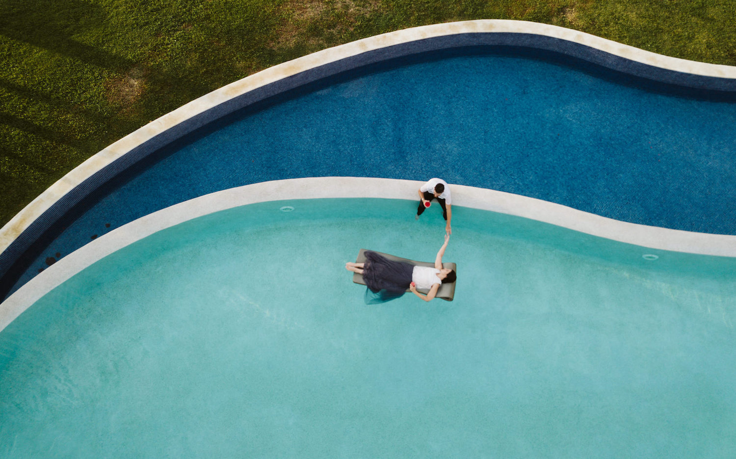 A person in a swimsuit and hat is floating on a pool float in a swimming pool, viewed from above.
