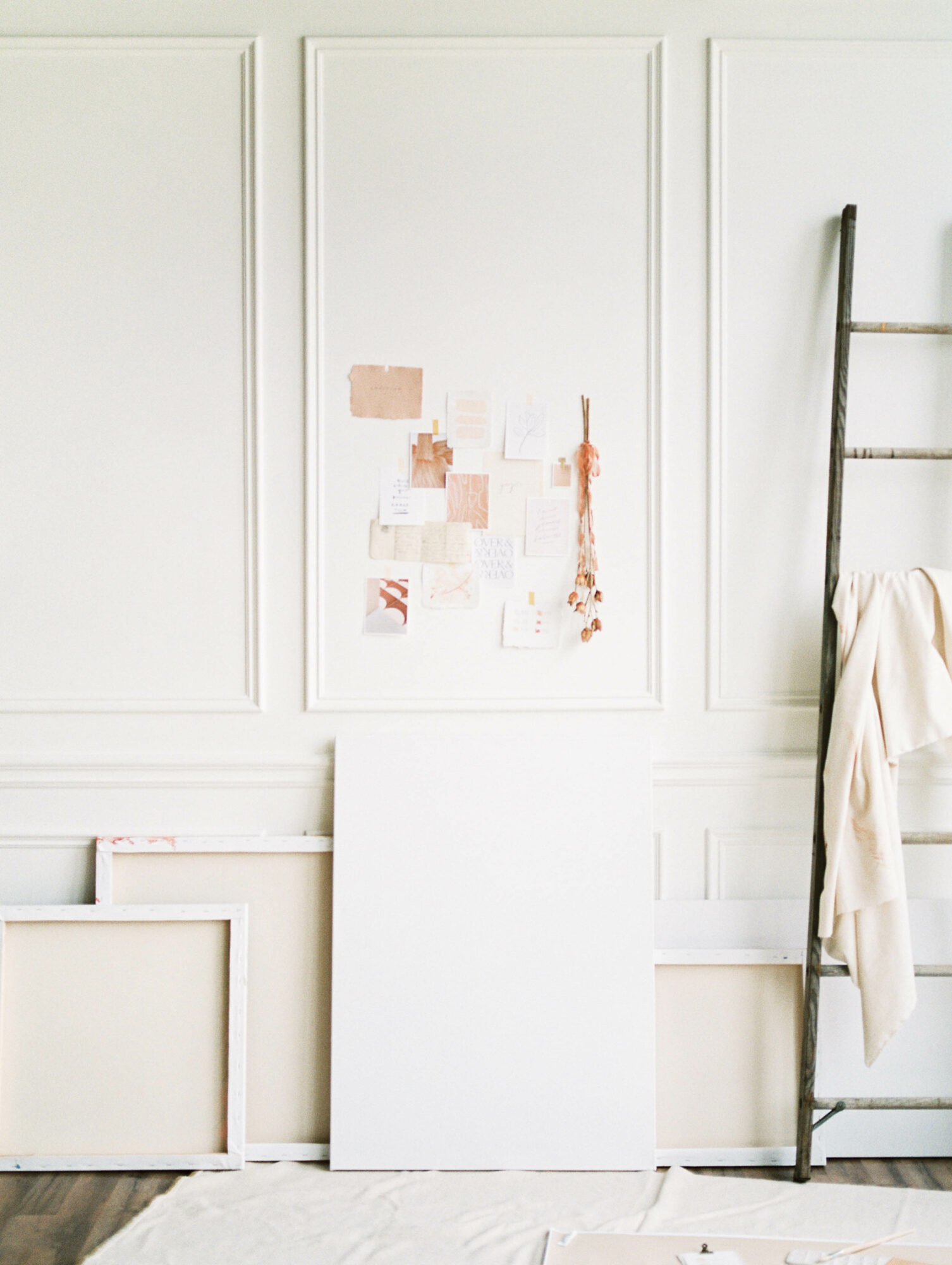 Empty room with white wall panels, a partially visible ladder, and a blank canvas leaning against the wall.