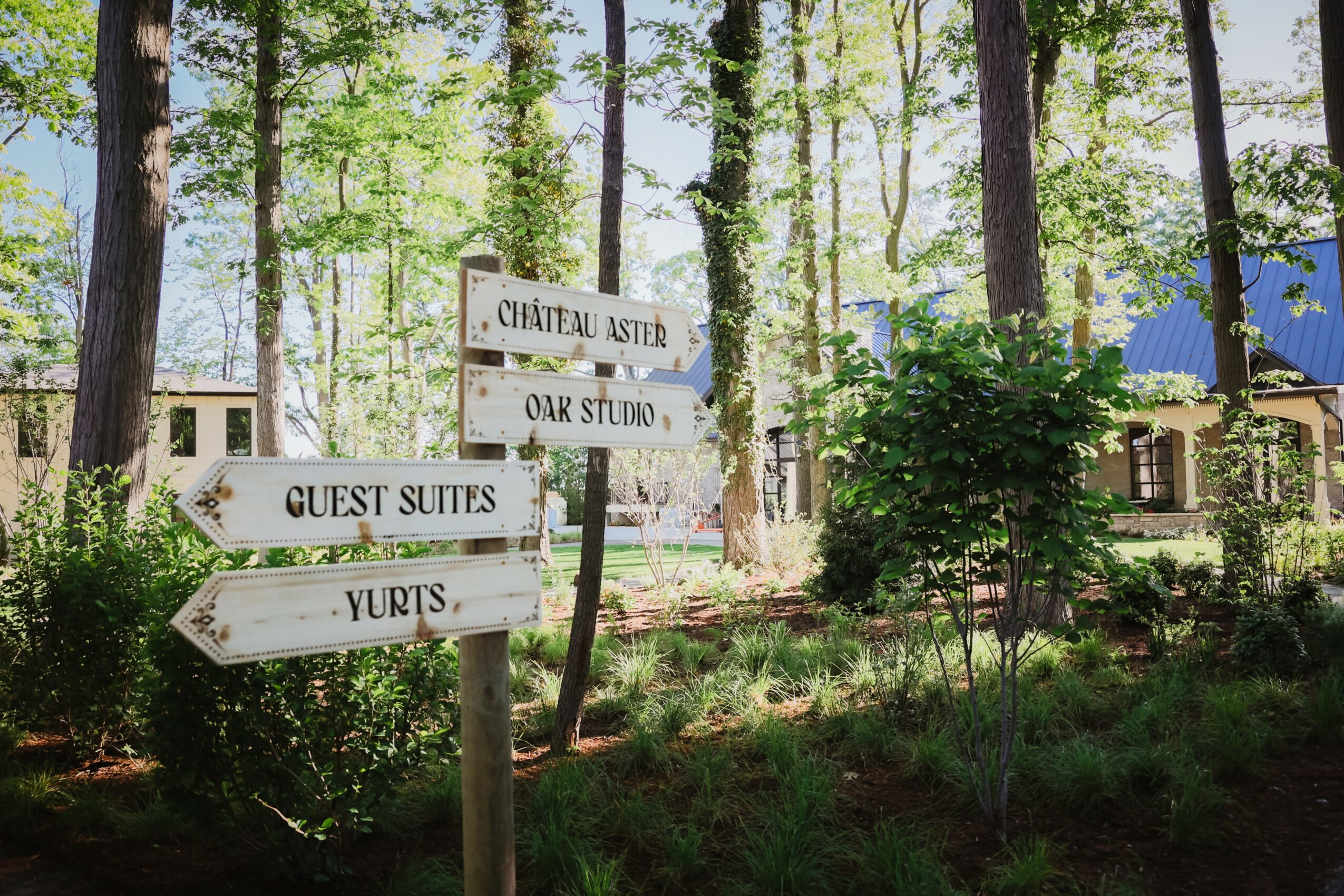 Wooden signpost with multiple directional signs in a forested area, pointing to guest suites, yurts, oak studio, and chateau Astud.
