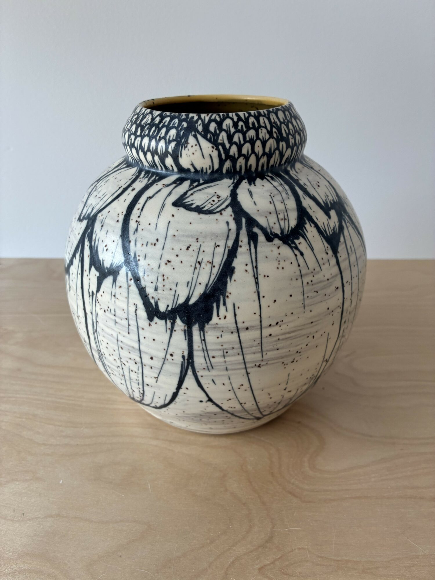 Round ceramic vase with black floral design on a light background, placed on a wooden surface.