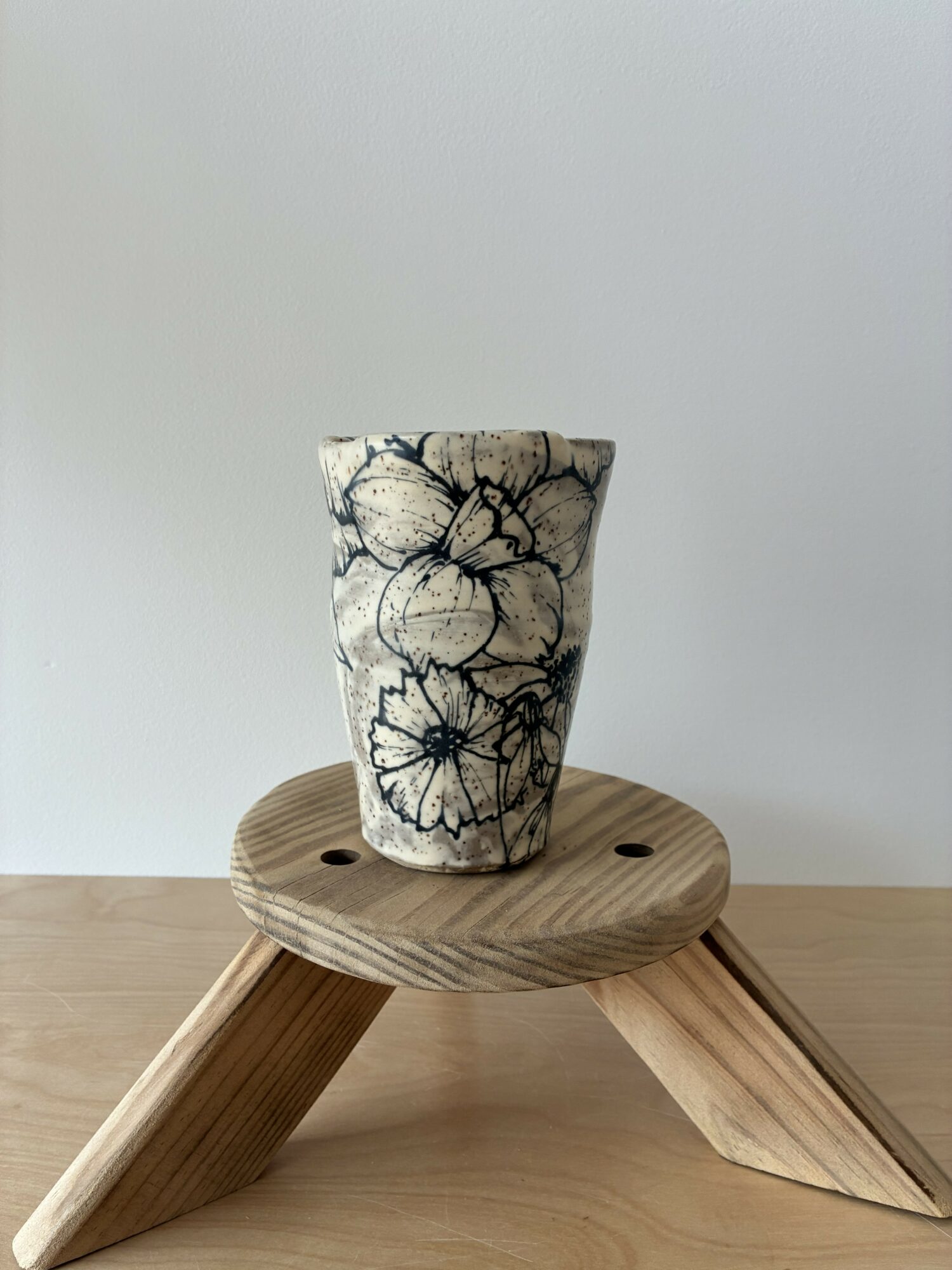 Ceramic vase with black floral pattern on a wooden round table against a plain background.