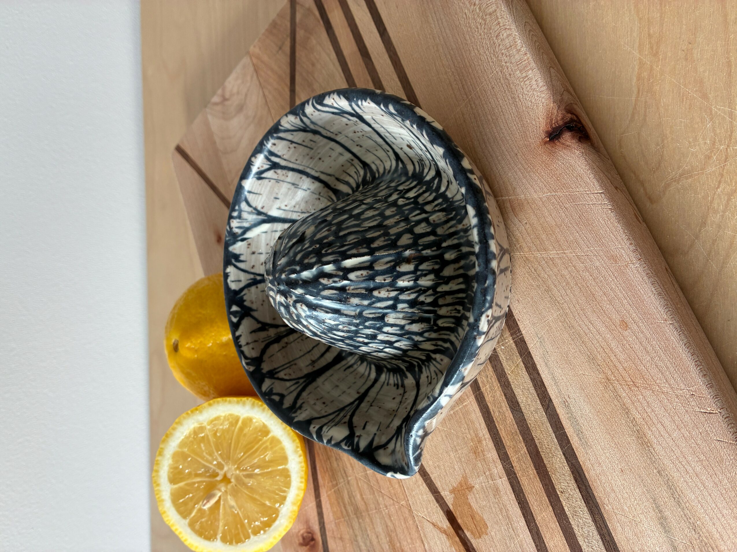 A lemon half, a yellow object, and a black and white patterned shell on a wooden surface.