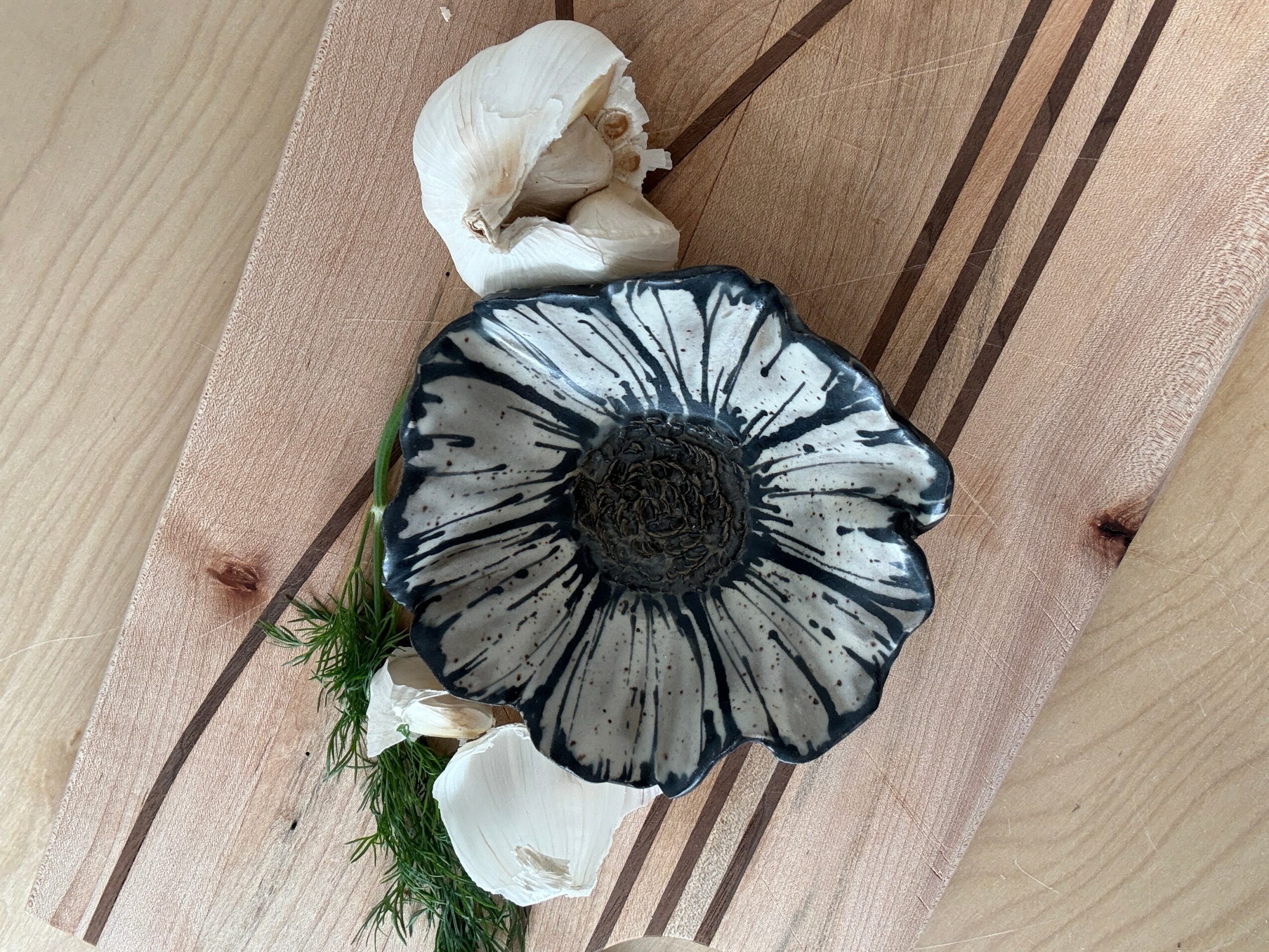 A black and white mushroom with a dark center, white flowers, and green moss on a wooden surface.