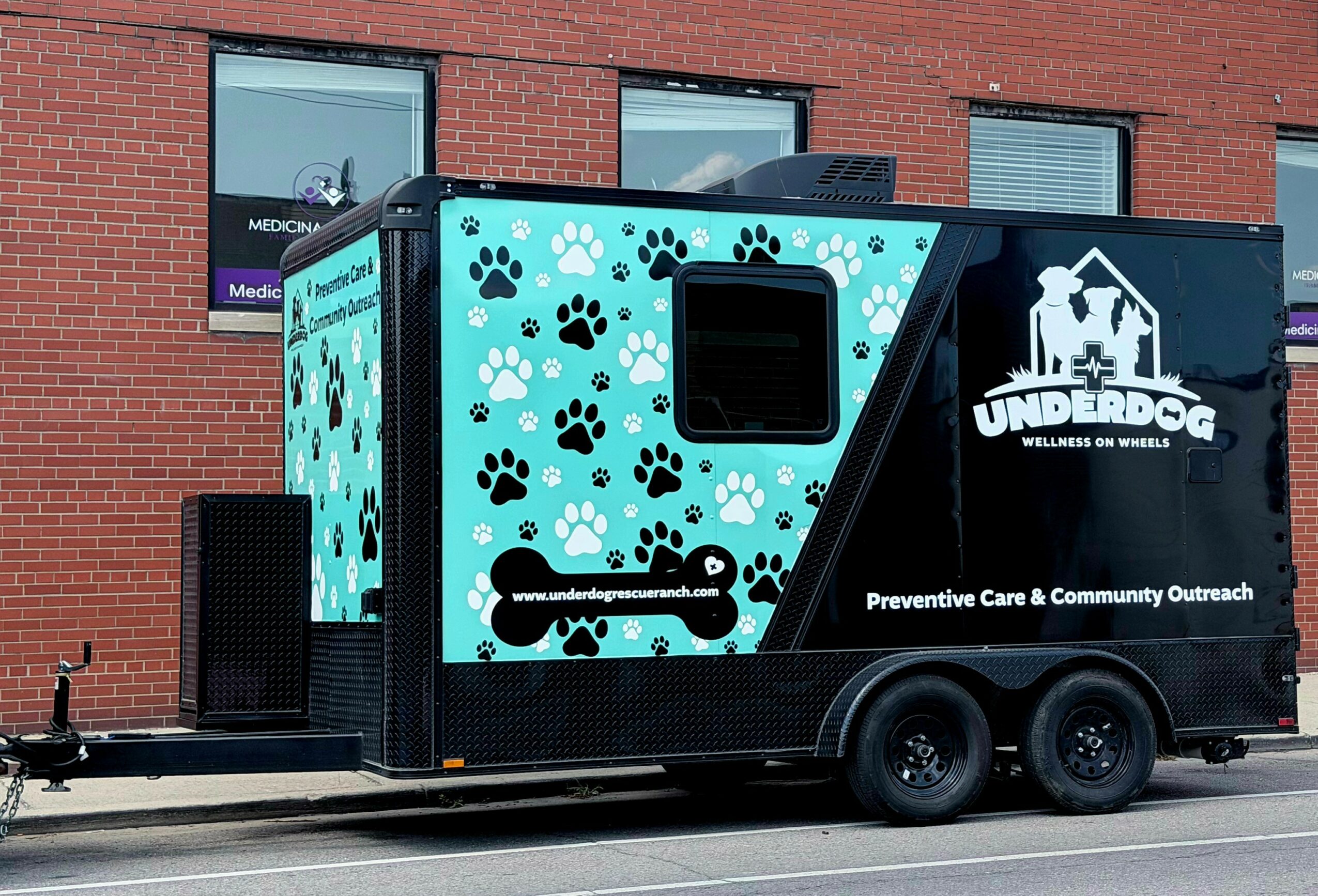 Mobile unit with paw print design and an underdog logo, parked on street, with brick building in background.
