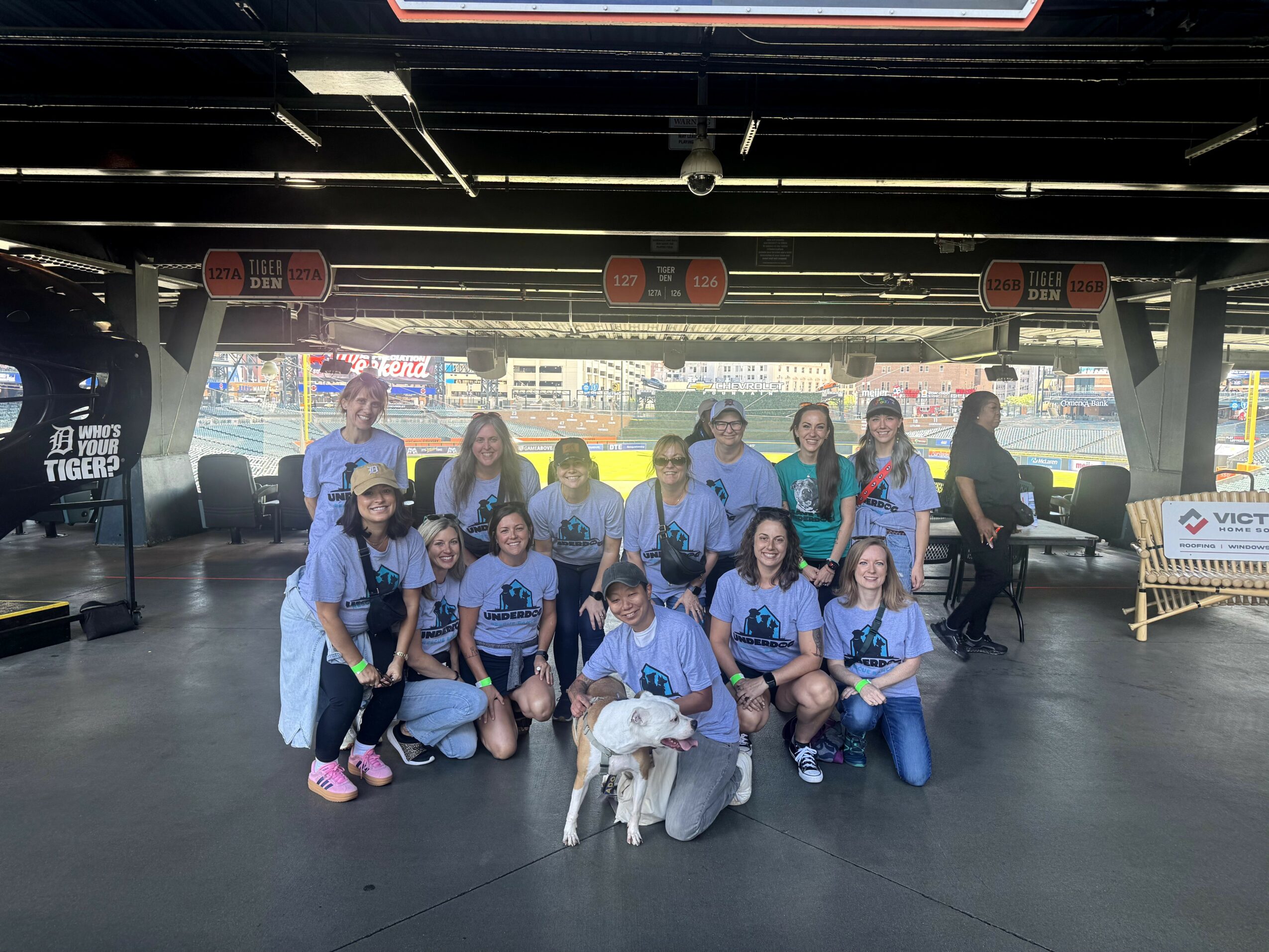 Group of people, including children and adults, posing with a dog in a covered outdoor area, with a cityscape in the background.
