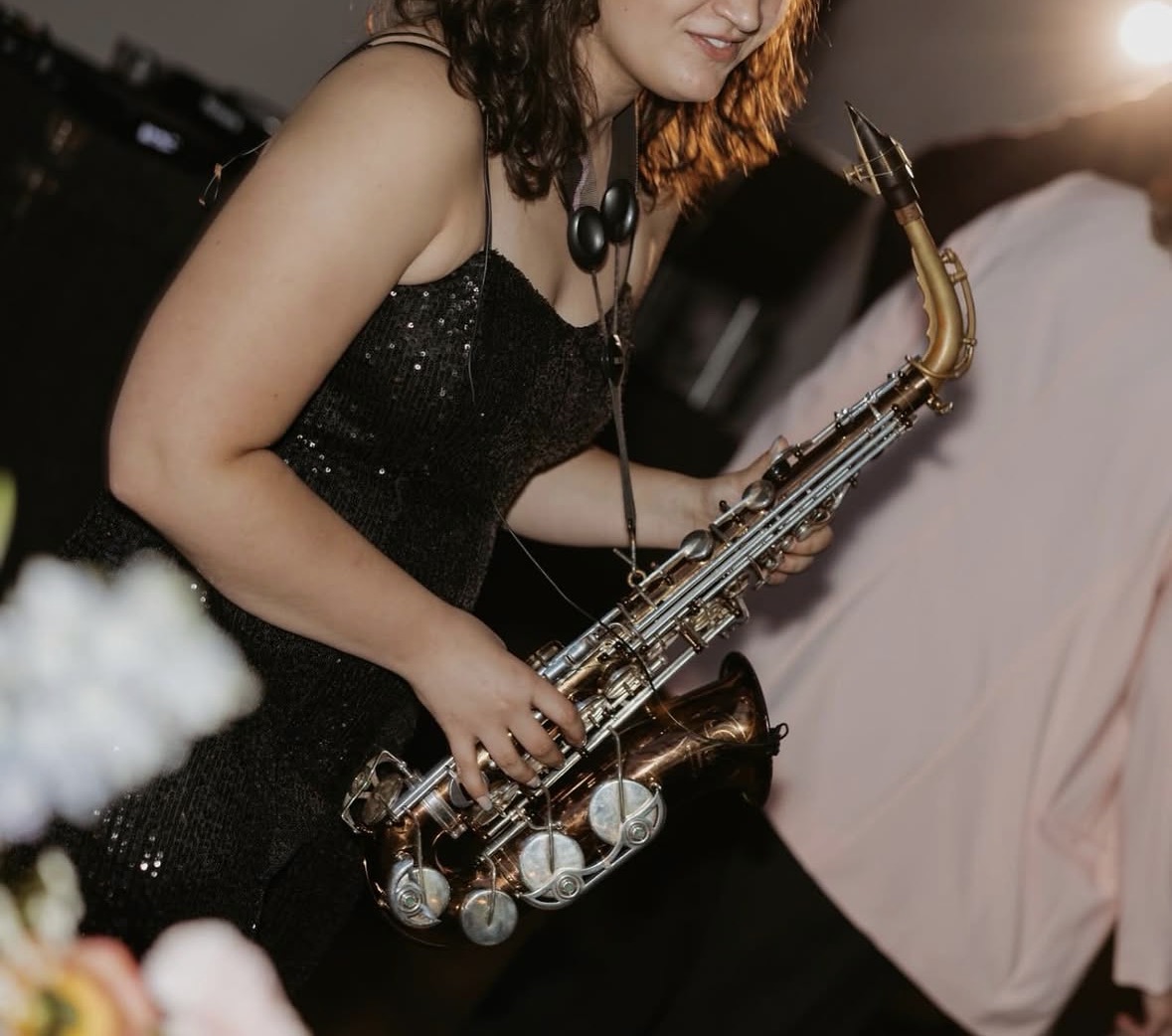Woman in black dress playing a saxophone at an outdoor event during sunset.