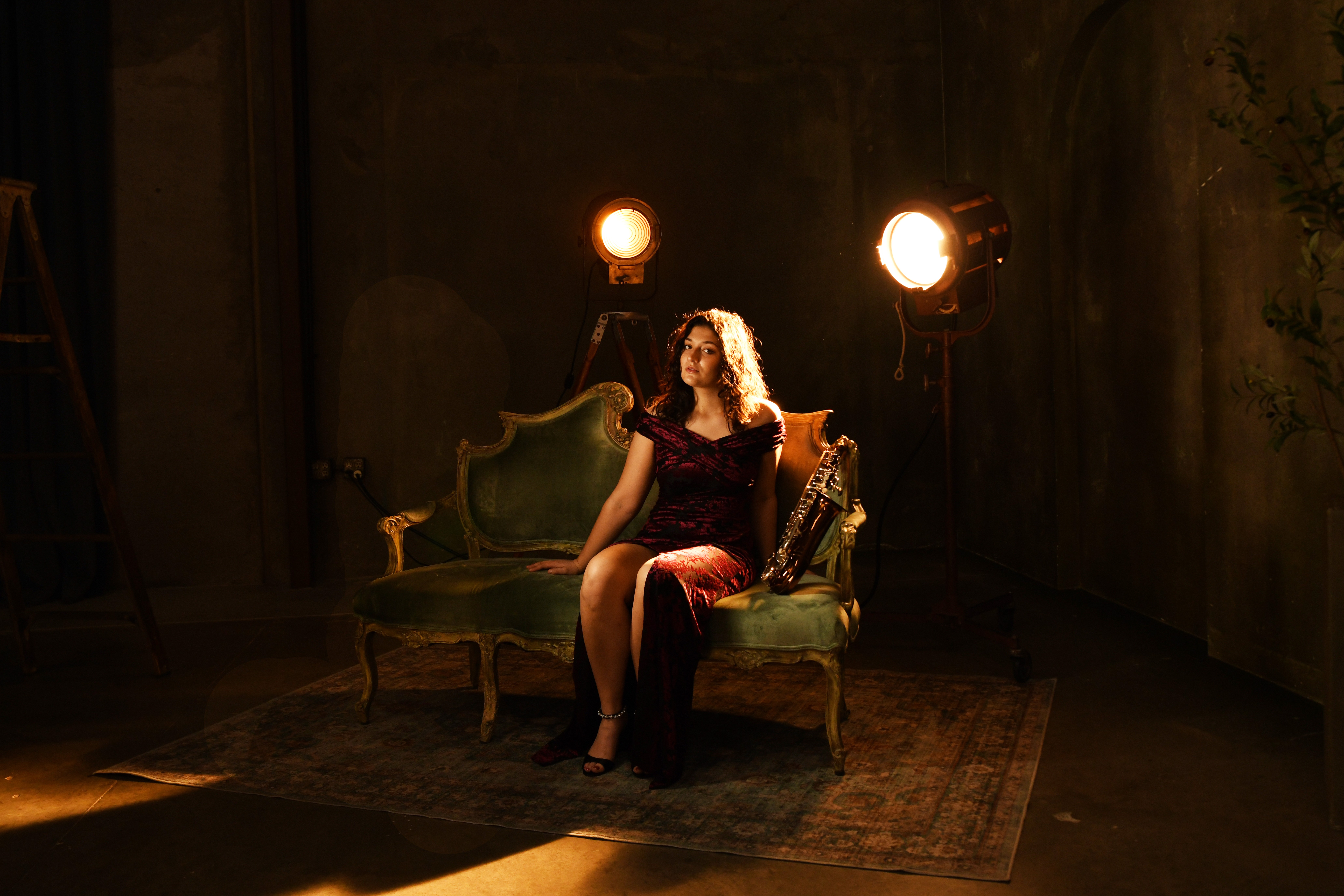 Woman sitting on a vintage green sofa in a dimly lit room with stage lights behind her.