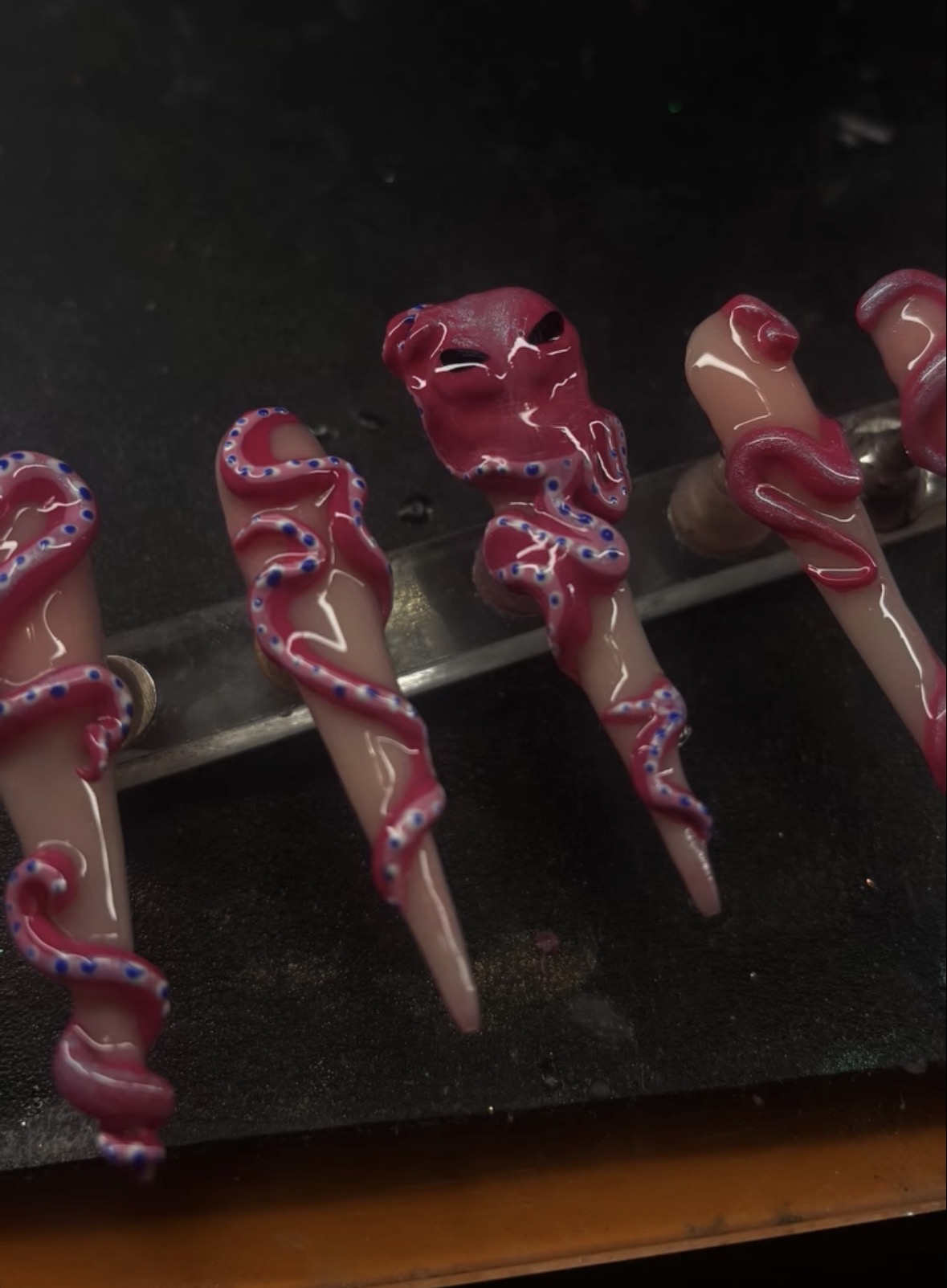 Five ice cream cones with pink and purple swirled icing, displayed on a dark surface.
