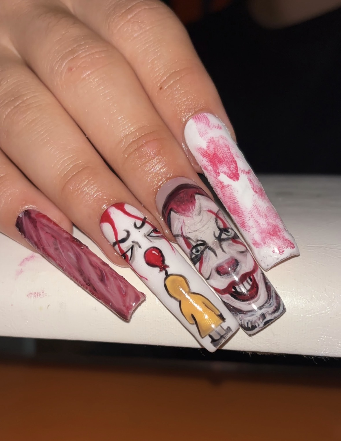 Nail art with a clown face, red and white colors, and a yellow balloon, on long decorated nails.