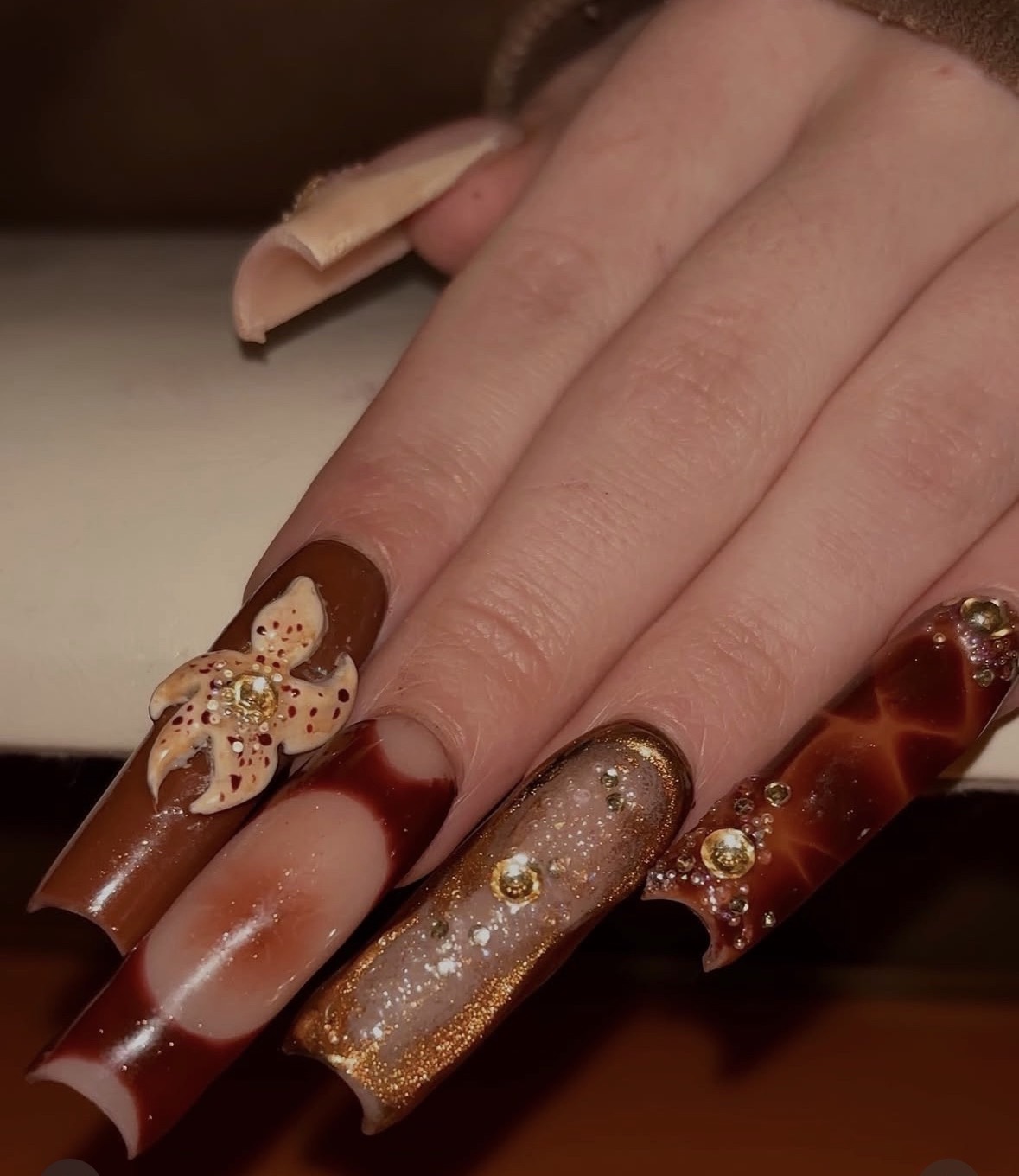 Close-up of a hand with decorated long nails featuring various designs and embellishments.