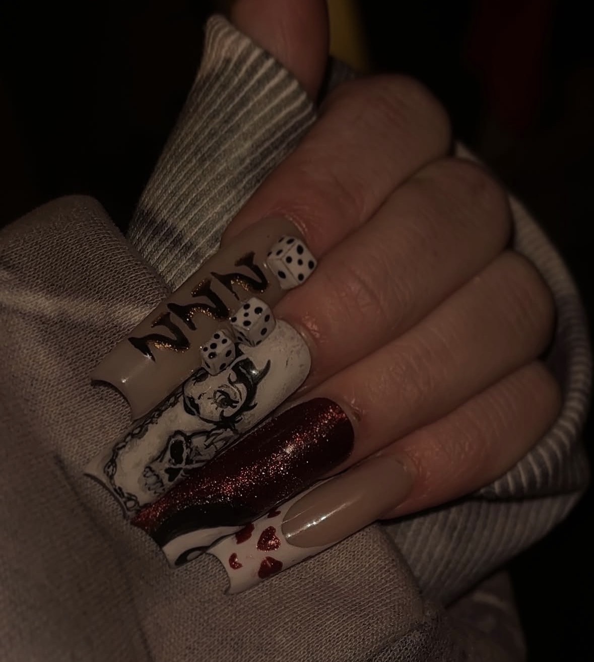 Close-up of a hand with decorated nails, some with white and black designs, one with red glitter, and one with red hearts.