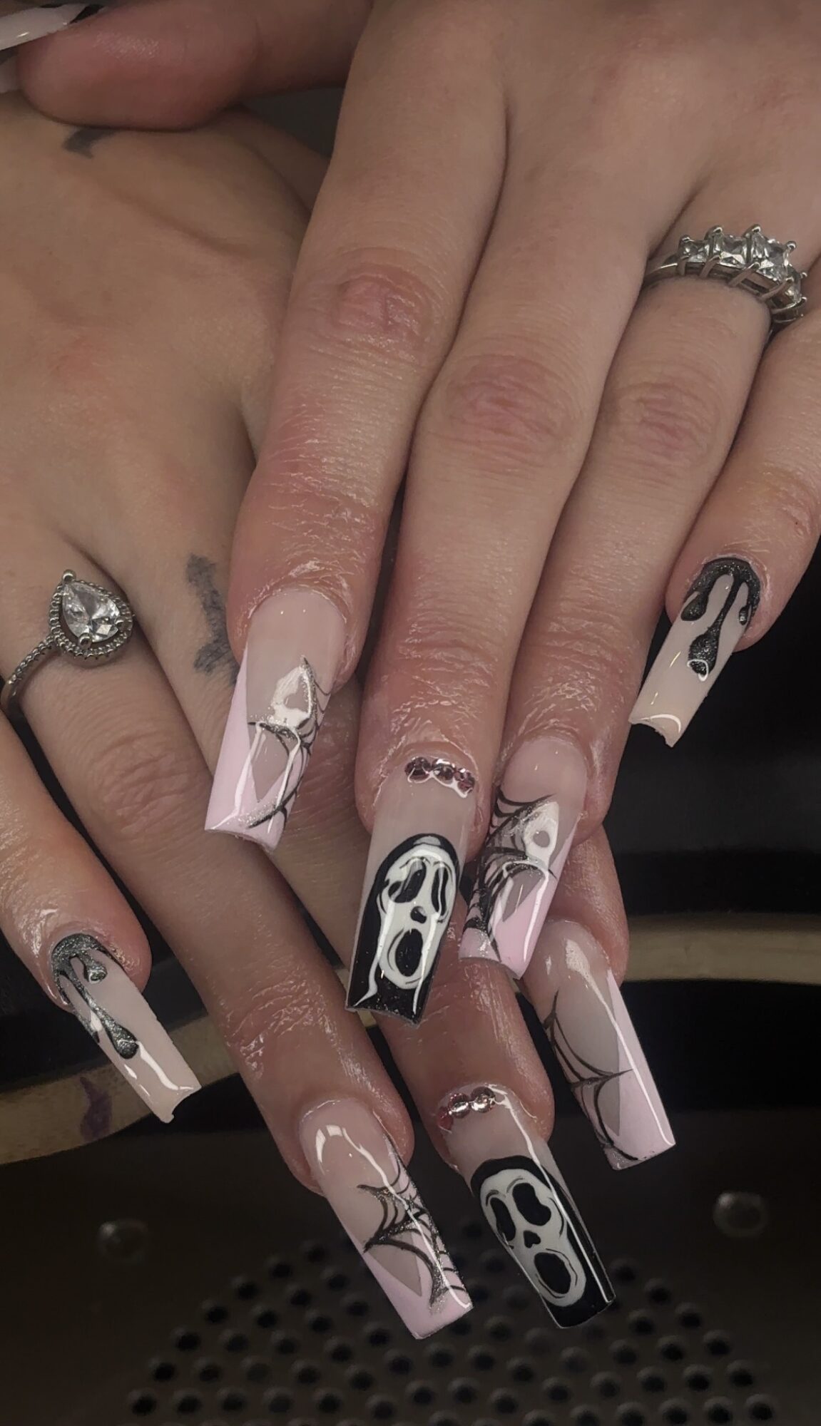Close-up of hands with long, decorated nails, rings, and visible skin texture.